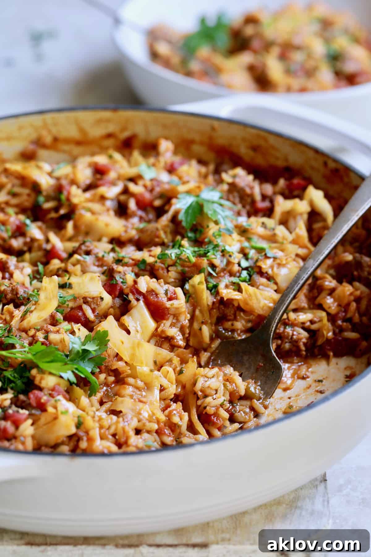 Serving spoonfuls of Unstuffed Chorizo Cabbage Roll Skillet from a white enamel skillet, highlighting the rich texture.