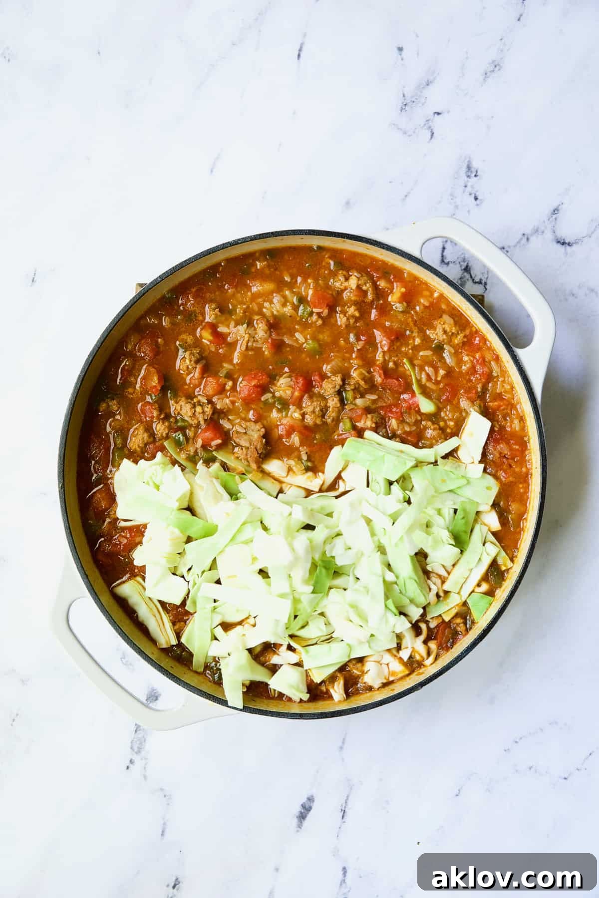 Raw sliced cabbage being added and stirred into the simmering Unstuffed Chorizo Cabbage Roll Skillet mixture.