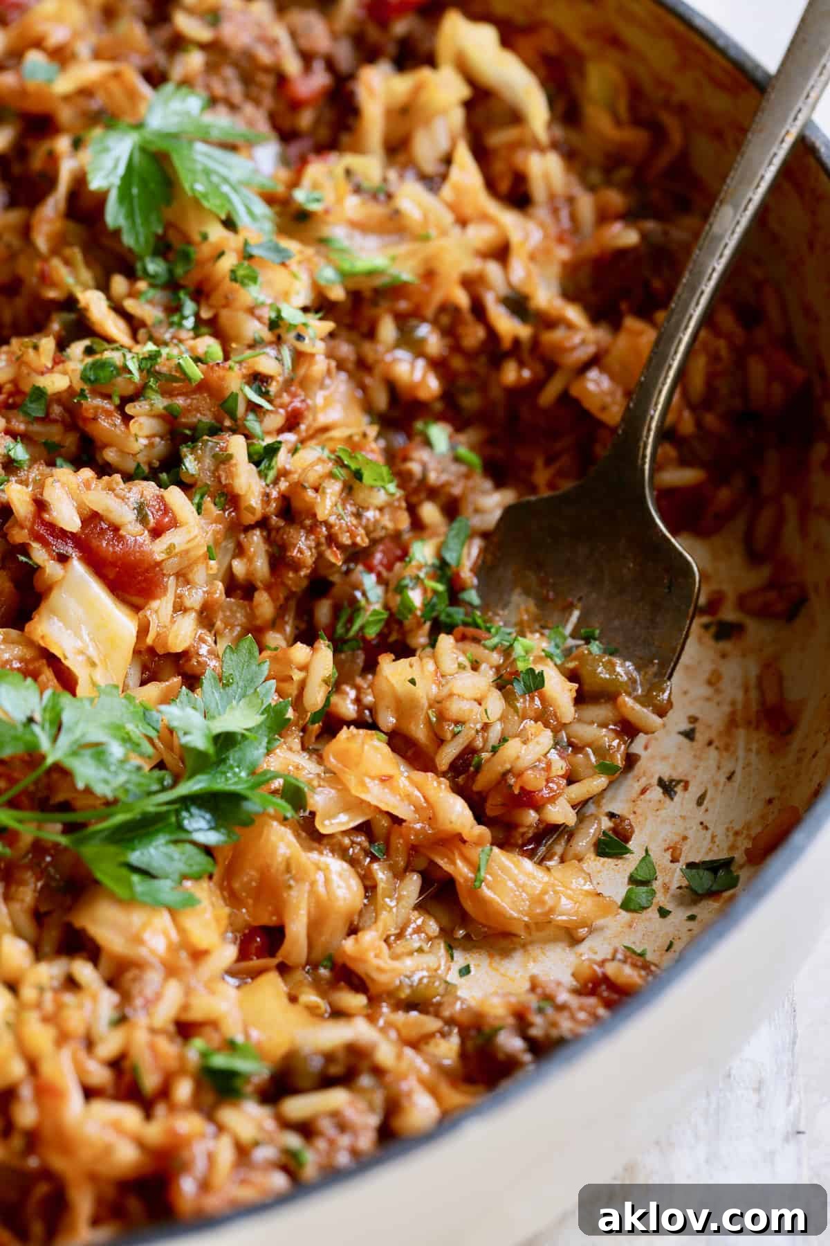 Close-up view of a serving of Unstuffed Chorizo Cabbage Roll Skillet on a plate with a fork, garnished with parsley, highlighting the texture.