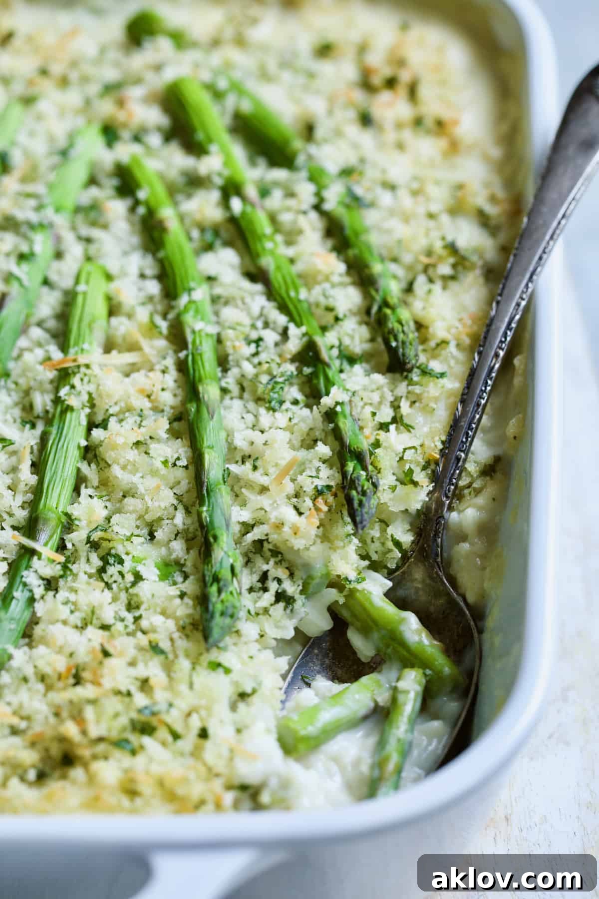 A close-up shot of the finished Creamy Asparagus and Rice Casserole in a white dish, with a serving spoon tucked into it, highlighting its texture and readiness to be served.
