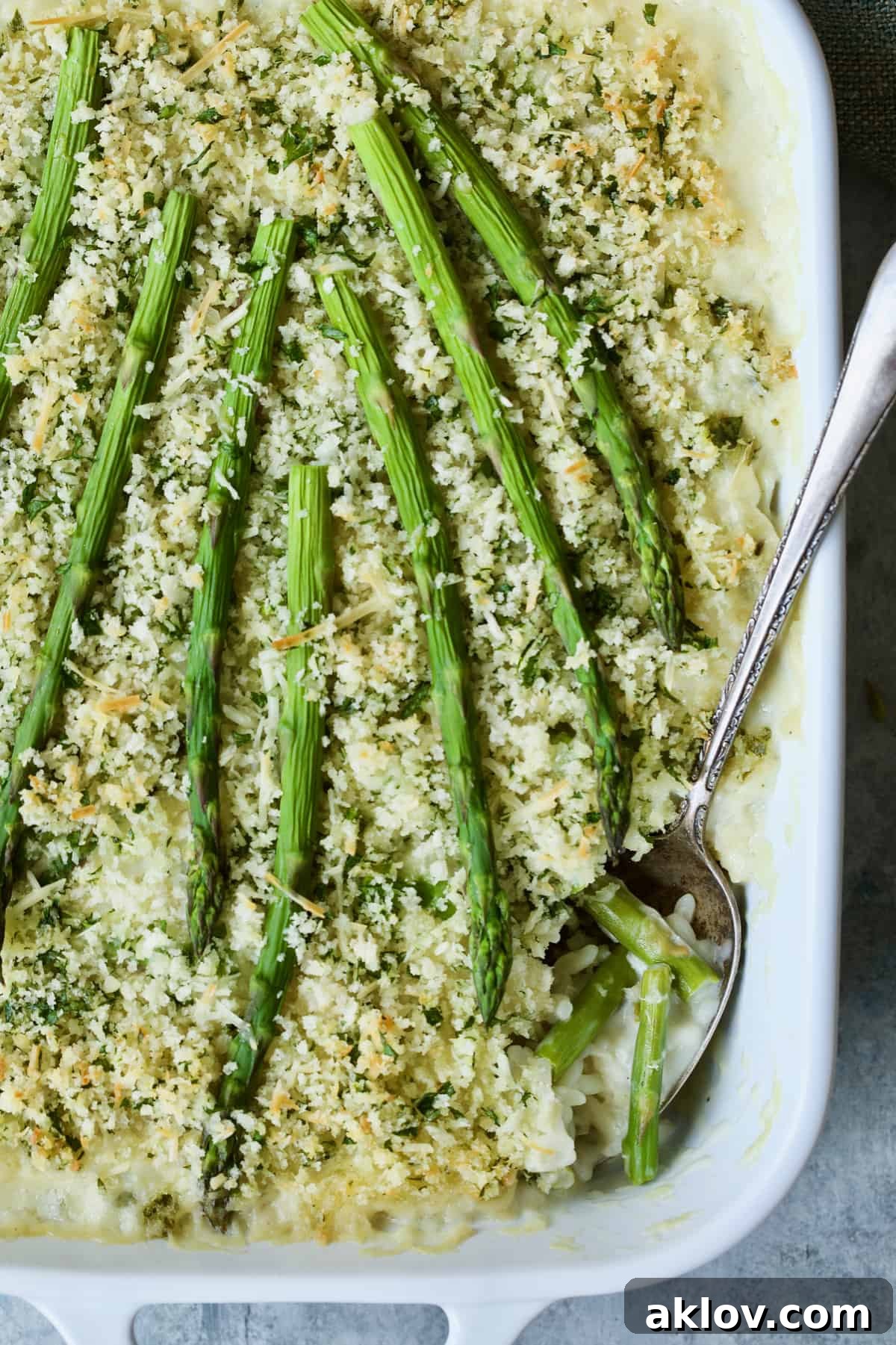 A generous serving of Creamy Asparagus and Rice Casserole being scooped from the baking dish with a serving spoon, showcasing its creamy interior.
