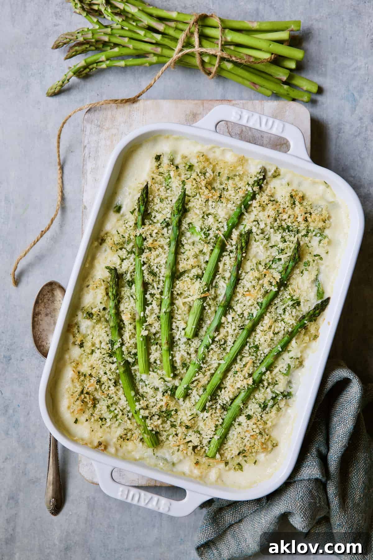 Close-up of Creamy Asparagus and Rice Casserole, with a serving spoon and a decorative bundle of asparagus tied with twine.
