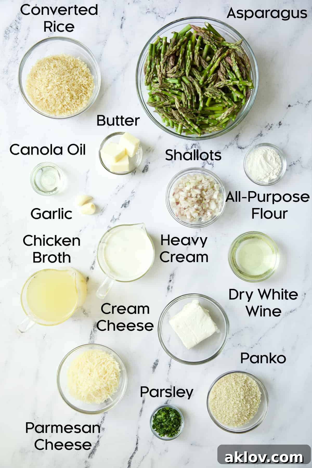 A flat lay photograph showcasing all the fresh ingredients for Creamy Asparagus and Rice Casserole laid out in glass bowls on a elegant marble background.