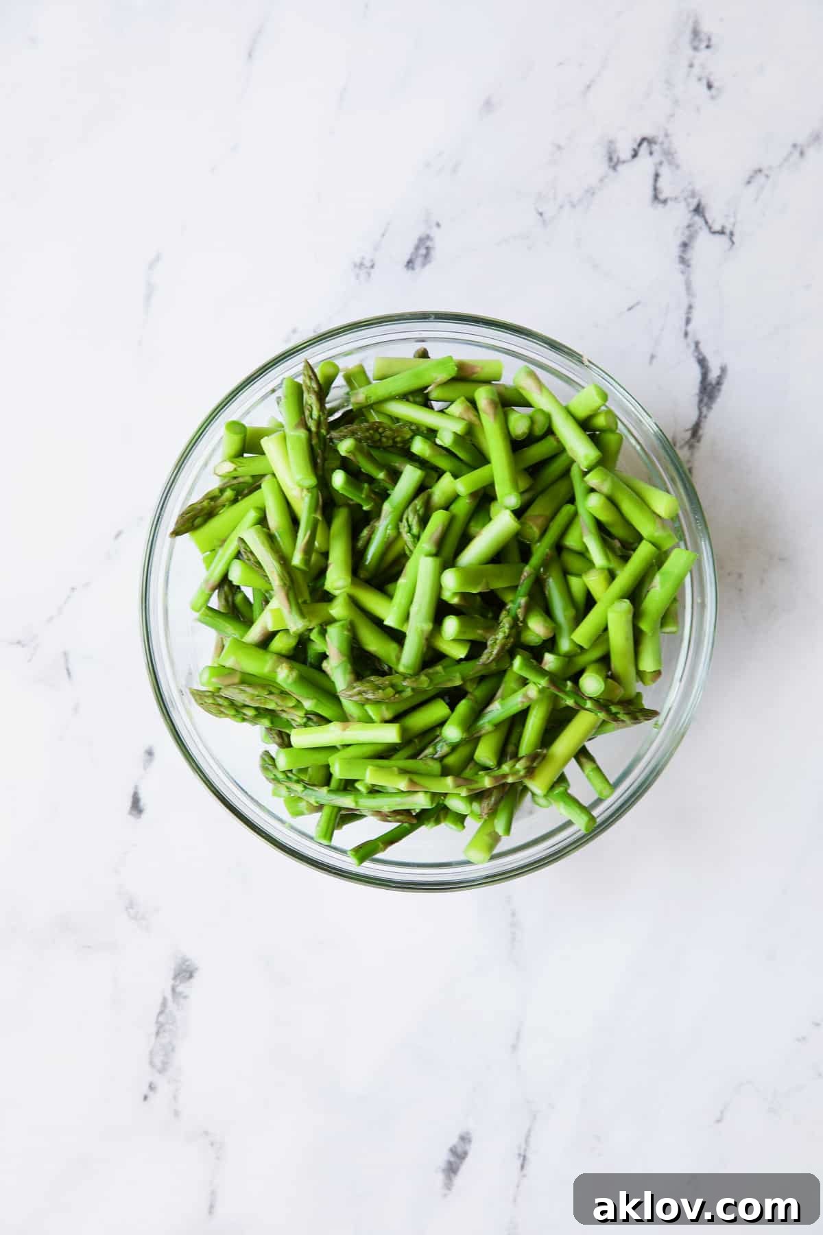Freshly blanched asparagus, bright green and crisp, resting in a clear glass bowl, ready for the next step of the casserole.