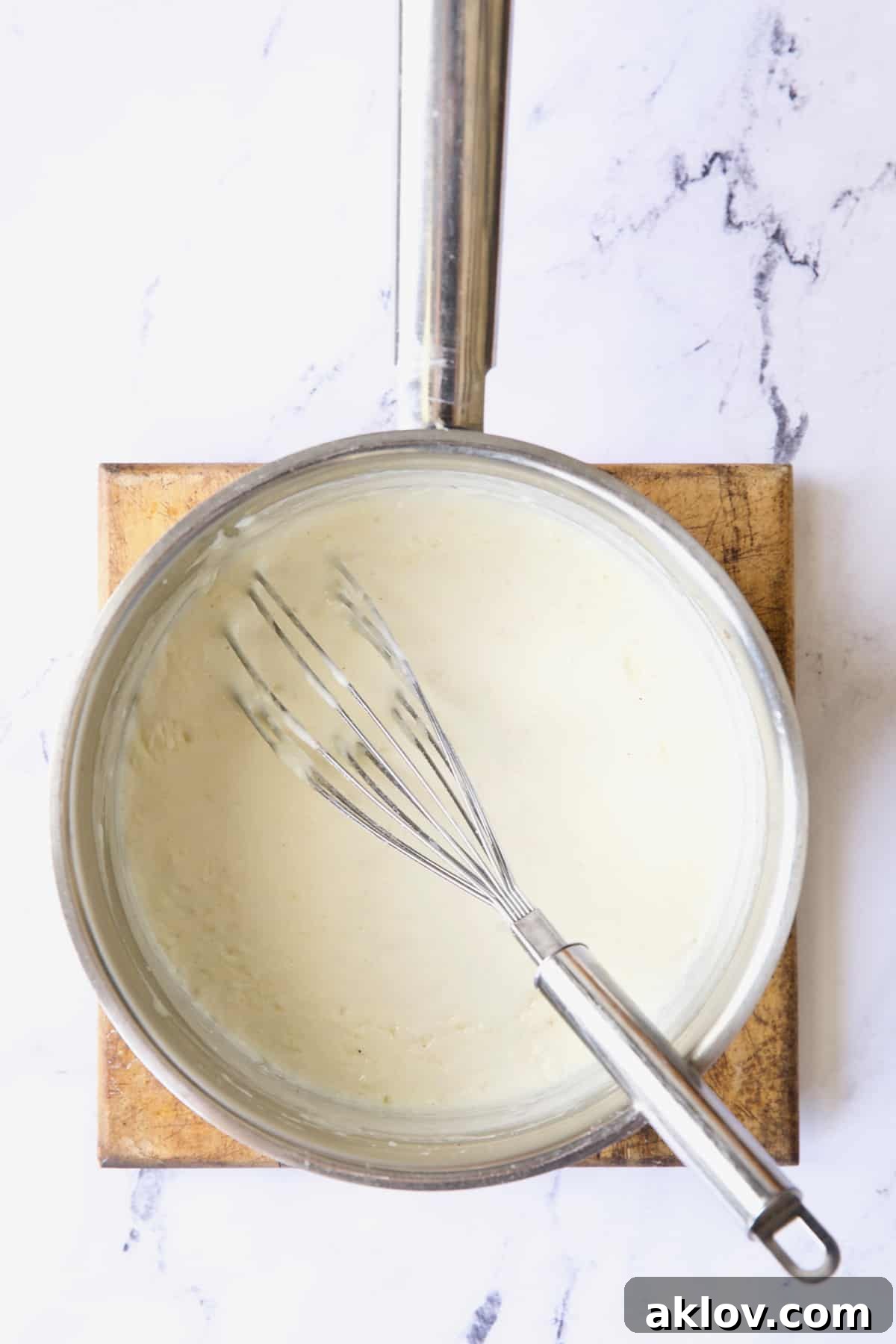 A close-up of the rich, creamy sauce simmering gently in a stainless steel saucepan, perfectly thickened and smooth.