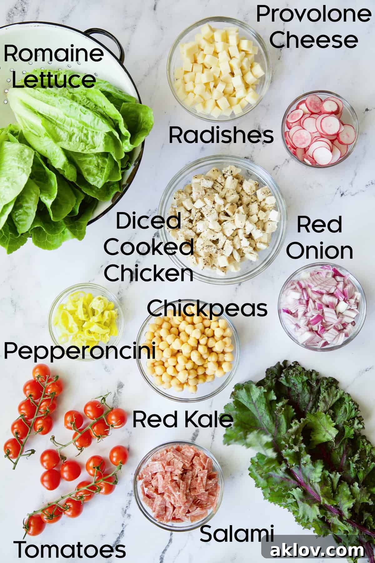 Fresh ingredients for Italian Chopped Salad with Chicken, including greens, tomatoes, and cheese, in glass bowls.