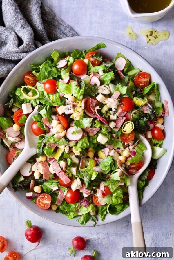 Photo of Italian Chopped Salad with Chicken in gray bowl with serving utensils.