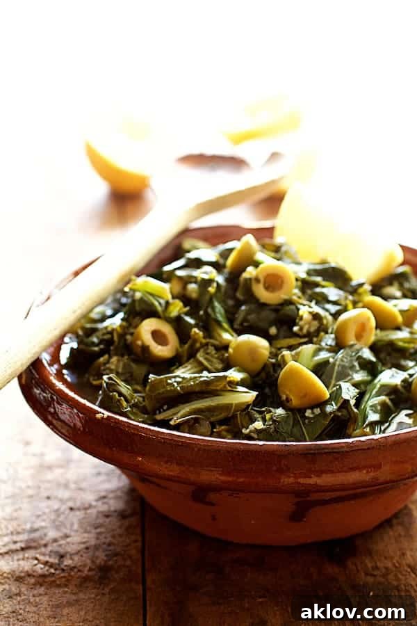 Close-up of Lemony Braised Greens with Olives served in a rustic clay bowl, garnished with lemon wedges and a serving spoon.