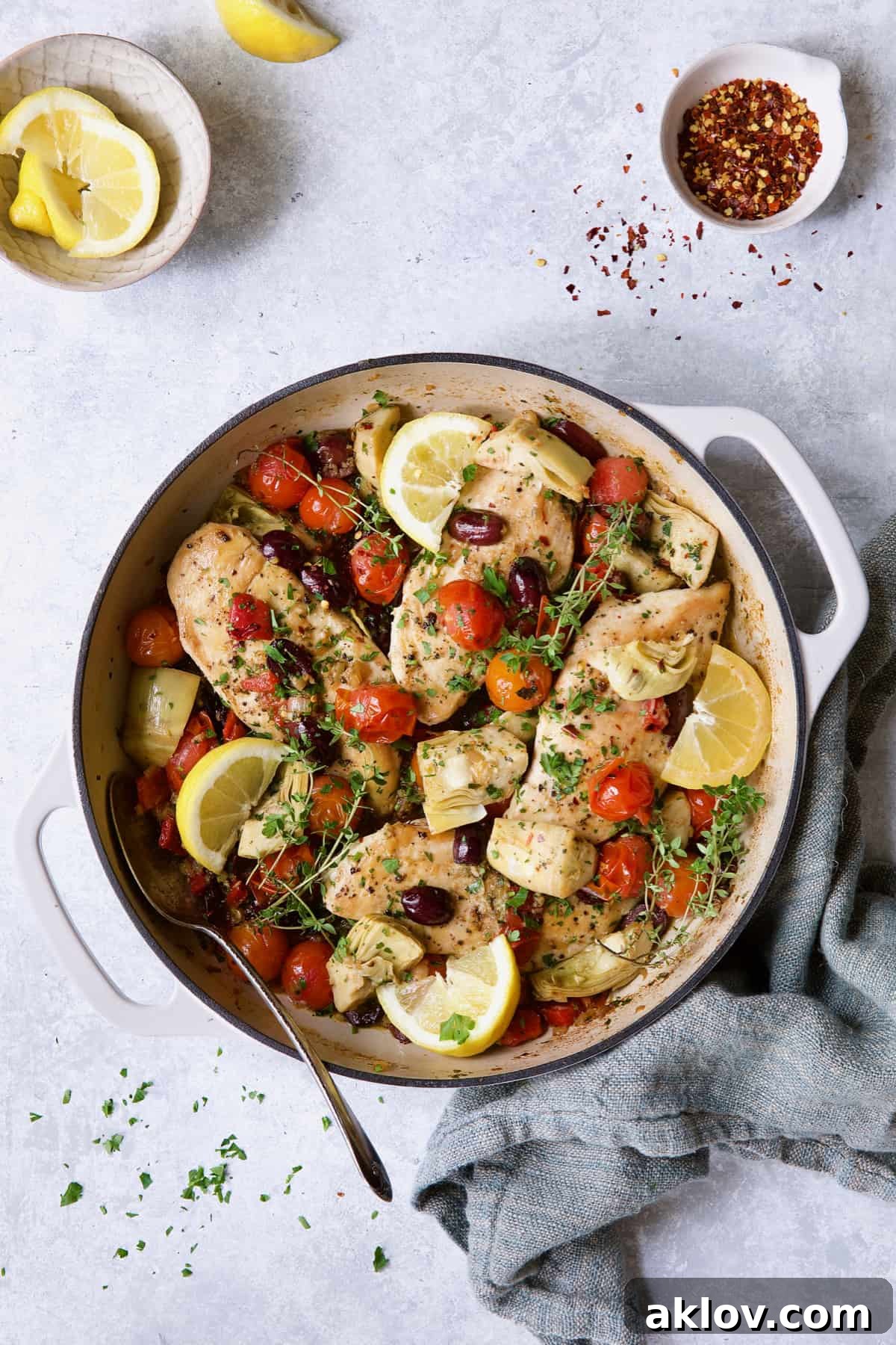 Easy Skillet Mediterranean Chicken on light blue background with blue towel garnished with lemon wedges and thyme.