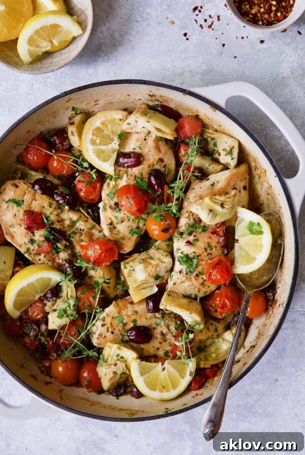Photo of Easy Skillet Mediterranean Chicken in white enamel cast iron skillet garnished with fresh thyme and lemon wedges.