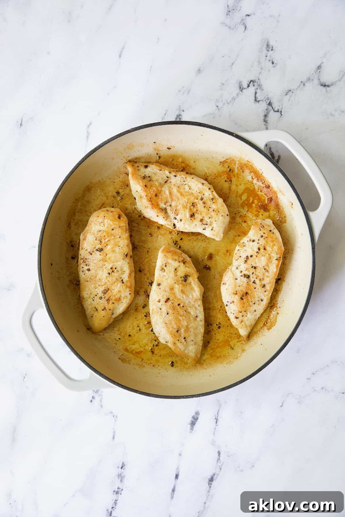 Four boneless skinless chicken breasts in white enamel skillet.