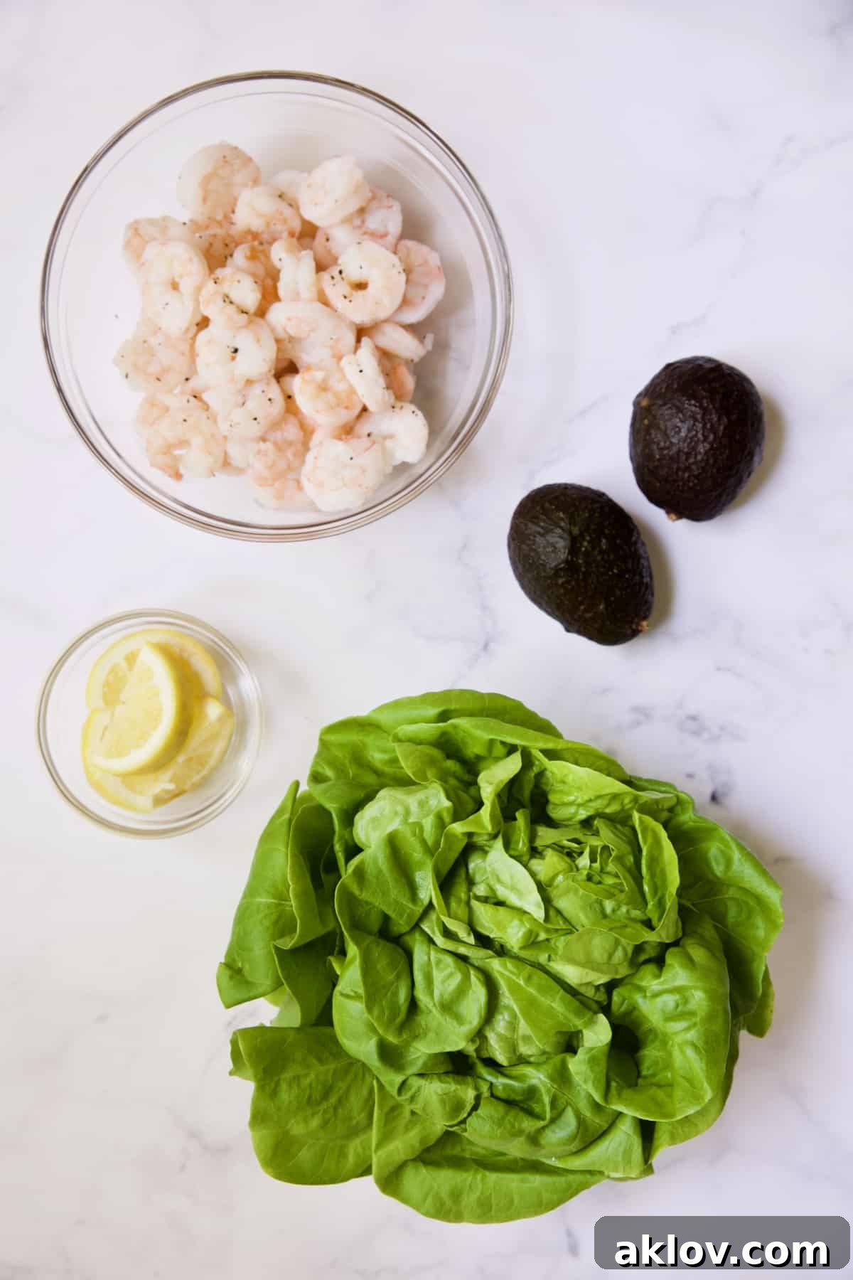 Photo of cooked shrimp, fresh lemon wedges, sliced avocados, and crisp lettuce leaves, ready for assembly.