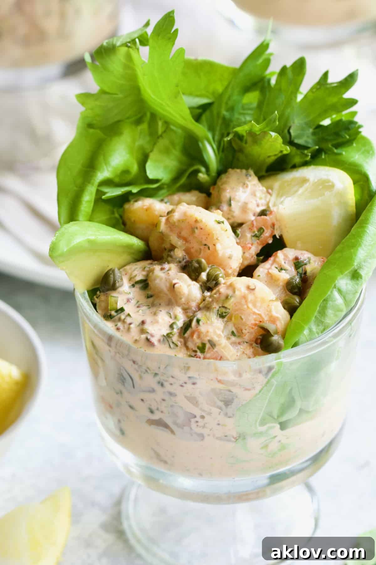 Sriracha Shrimp Remoulade Cocktail in footed glass with avocado, lemon, lettuce and celery sprigs.