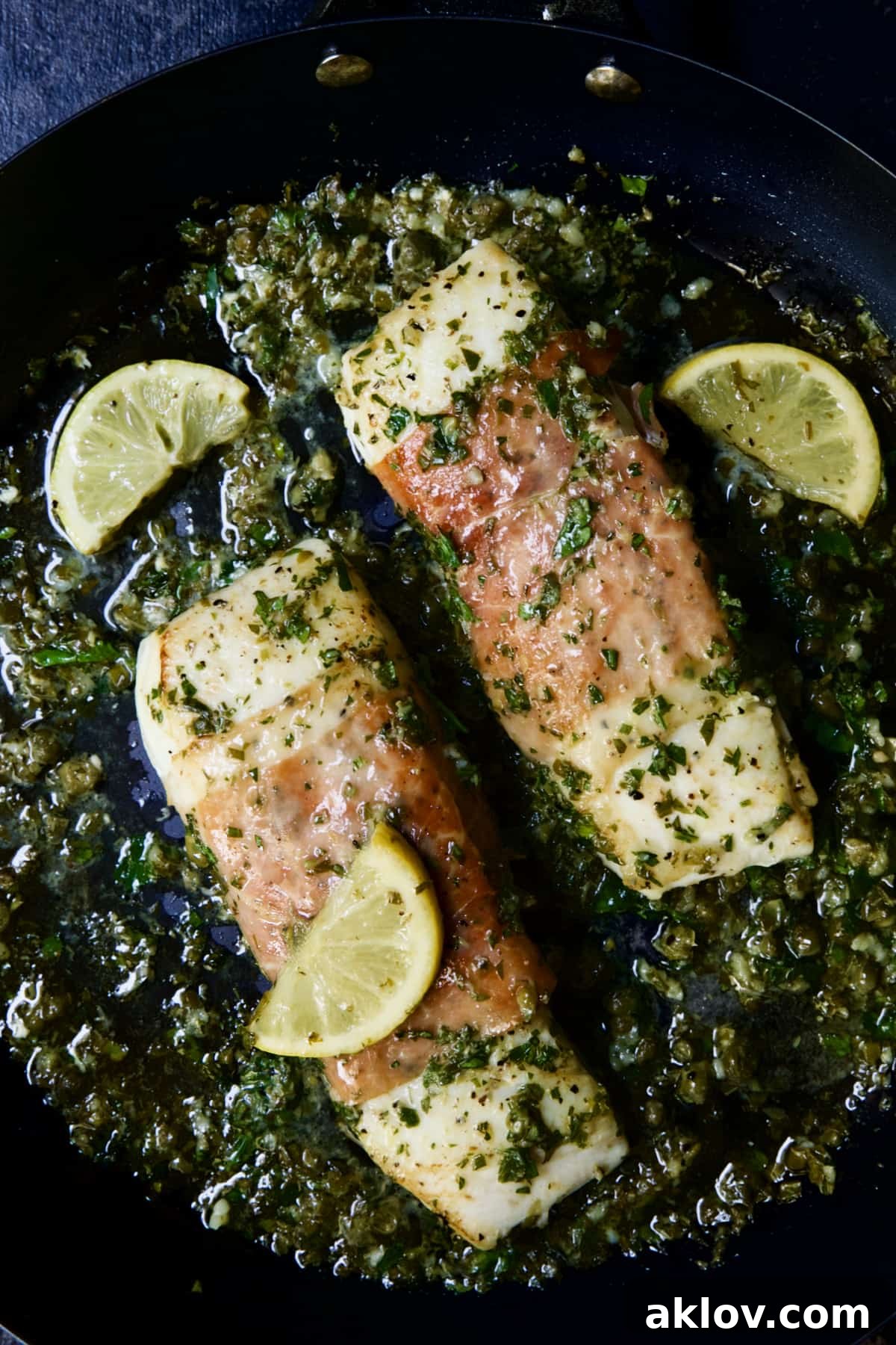 Prosciutto-Wrapped Halibut with Herb - Caper Butter with lemon wedges.