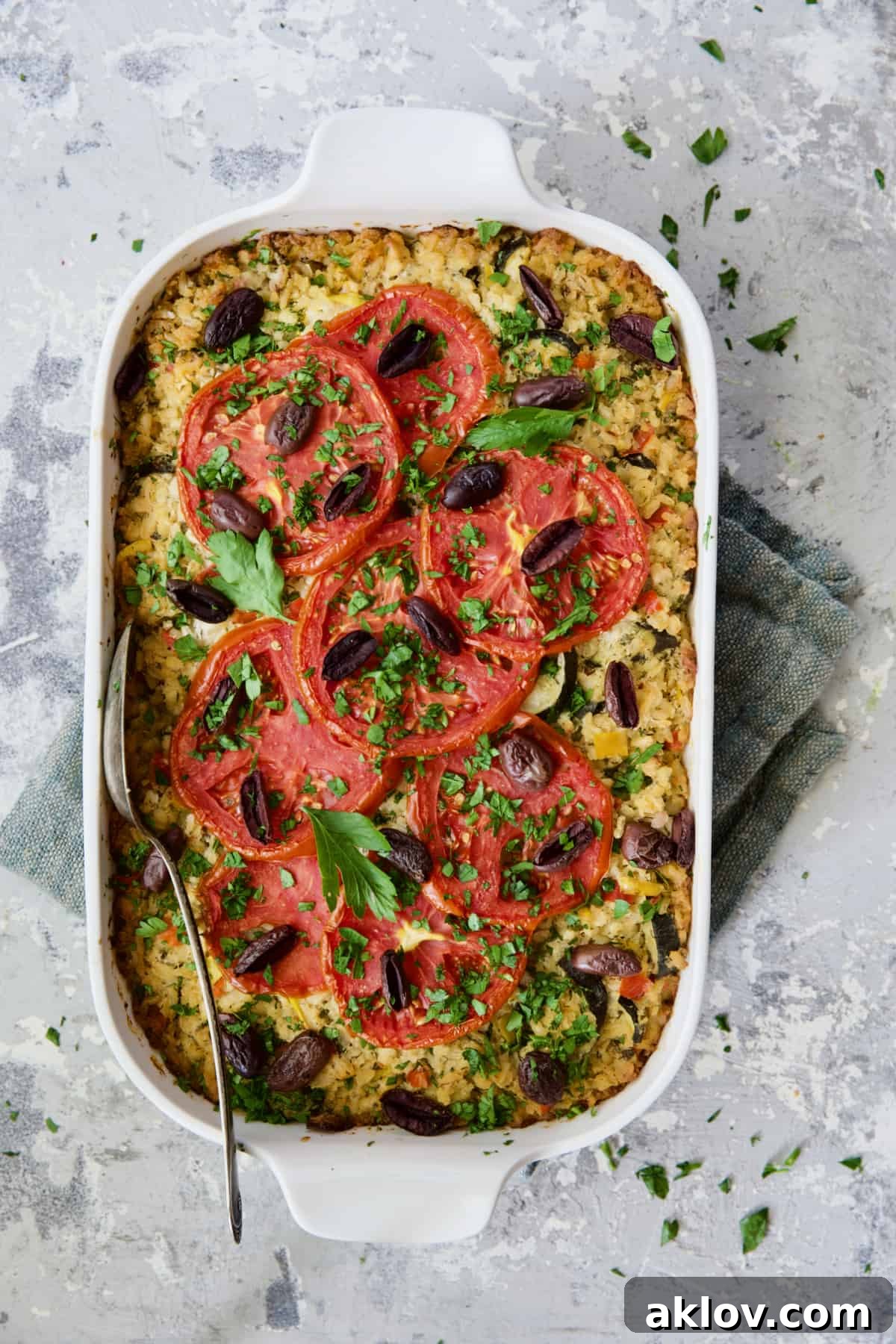 A beautifully baked Greek Brown Rice and Vegetable Casserole, garnished with fresh parsley, with a serving spoon on a blue napkin, ready to be enjoyed.