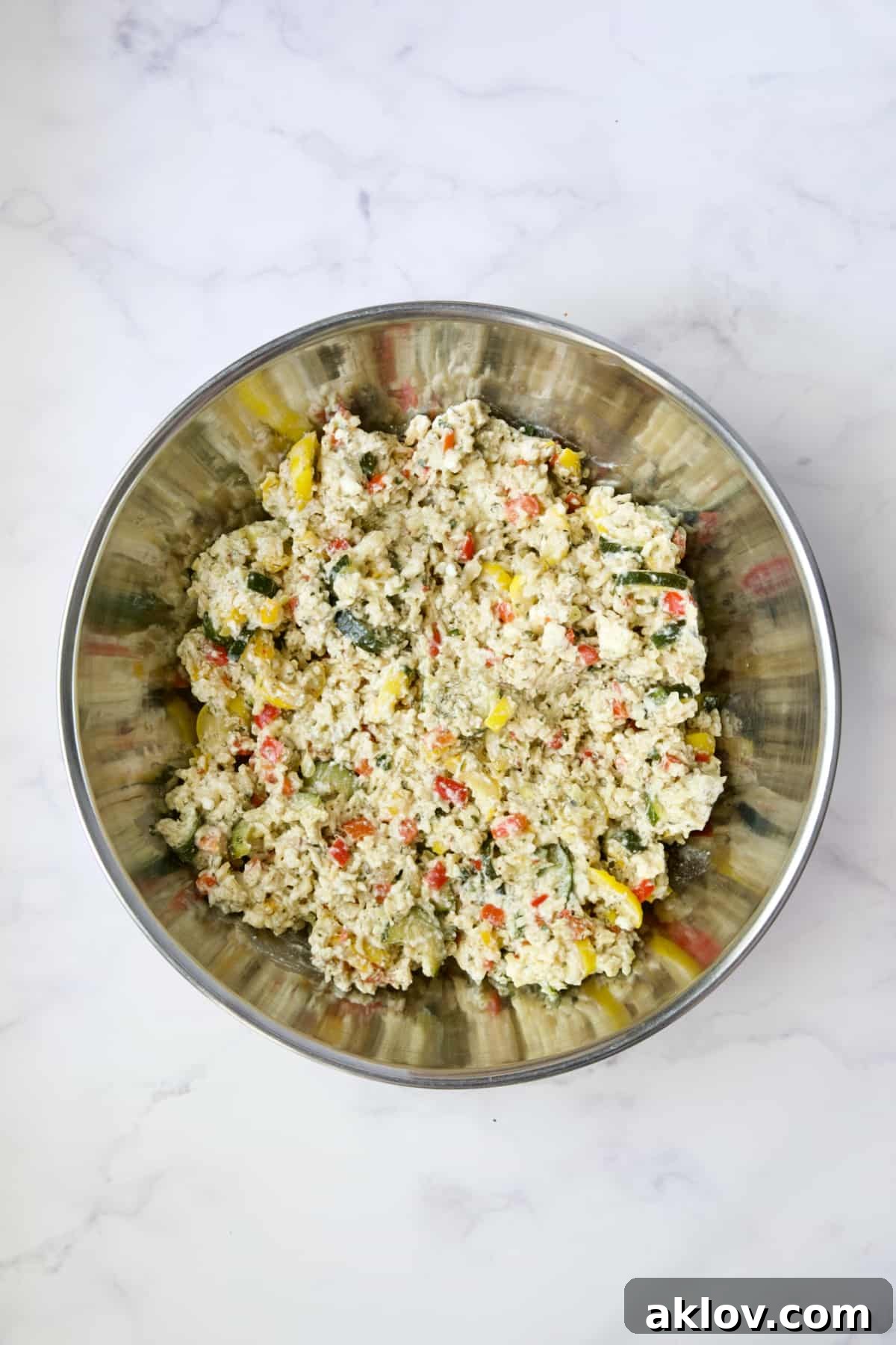 All ingredients for Greek Brown Rice and Vegetable Casserole thoroughly stirred together in a stainless steel bowl, ready for baking.