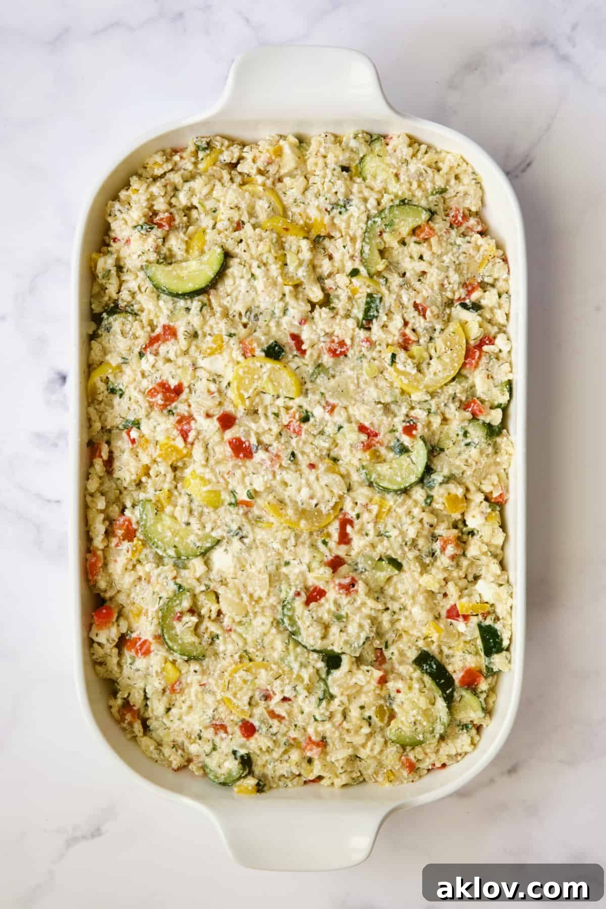 Assembled Greek Brown Rice and Vegetable Casserole in baking dish, before the final topping of fresh tomatoes and black olives.