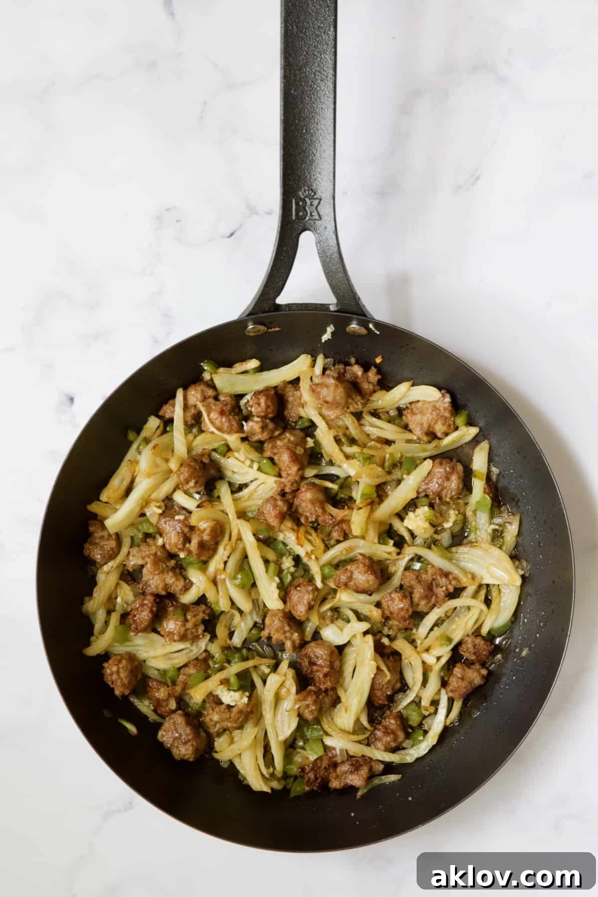 Molten Sunset Eggs 6 Sautéed Italian sausage, fennel, onions, and green bell pepper mixed together in a black skillet, creating a vibrant base for the sauce.