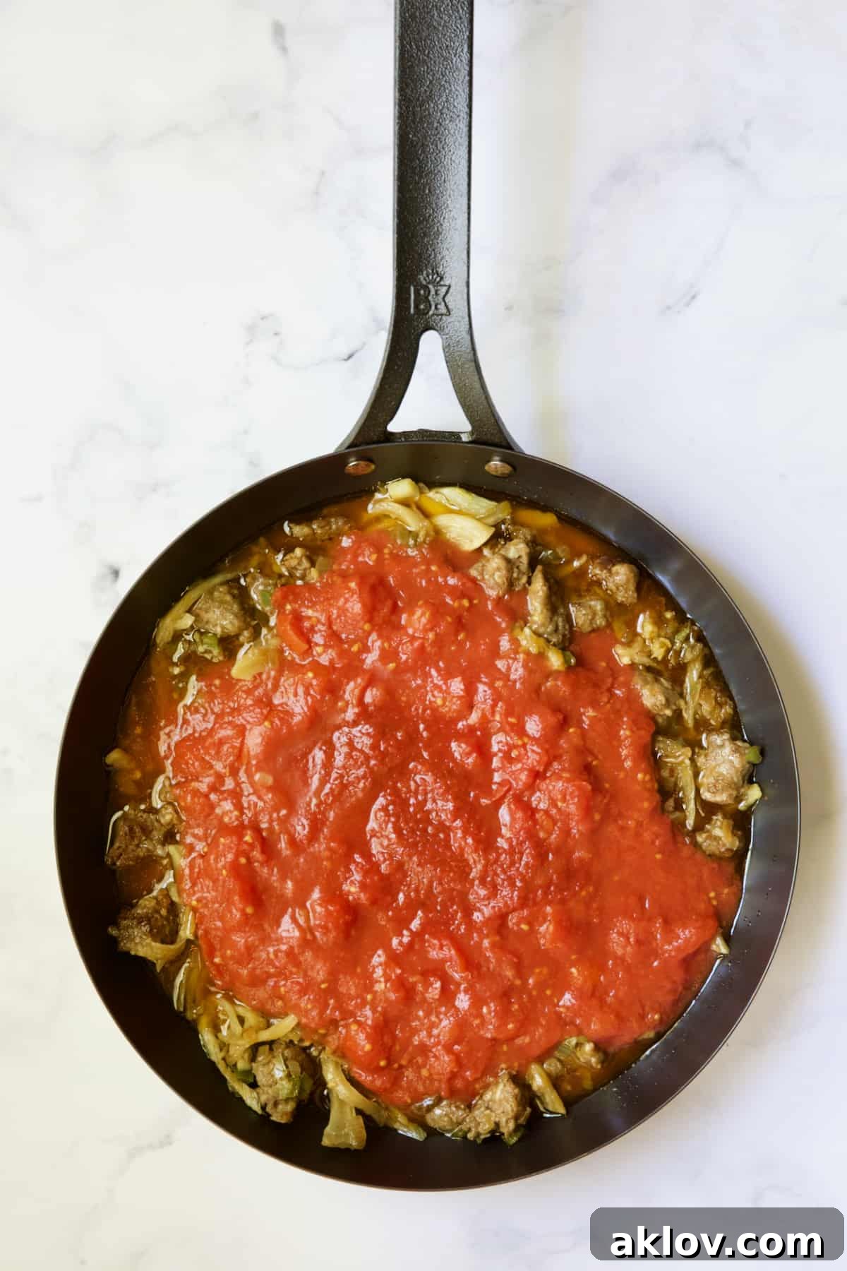 Molten Sunset Eggs 7 Rich tomato sauce and spicy chili paste added to the cooked Italian sausage and vegetables in a black skillet, beginning to simmer and meld flavors.