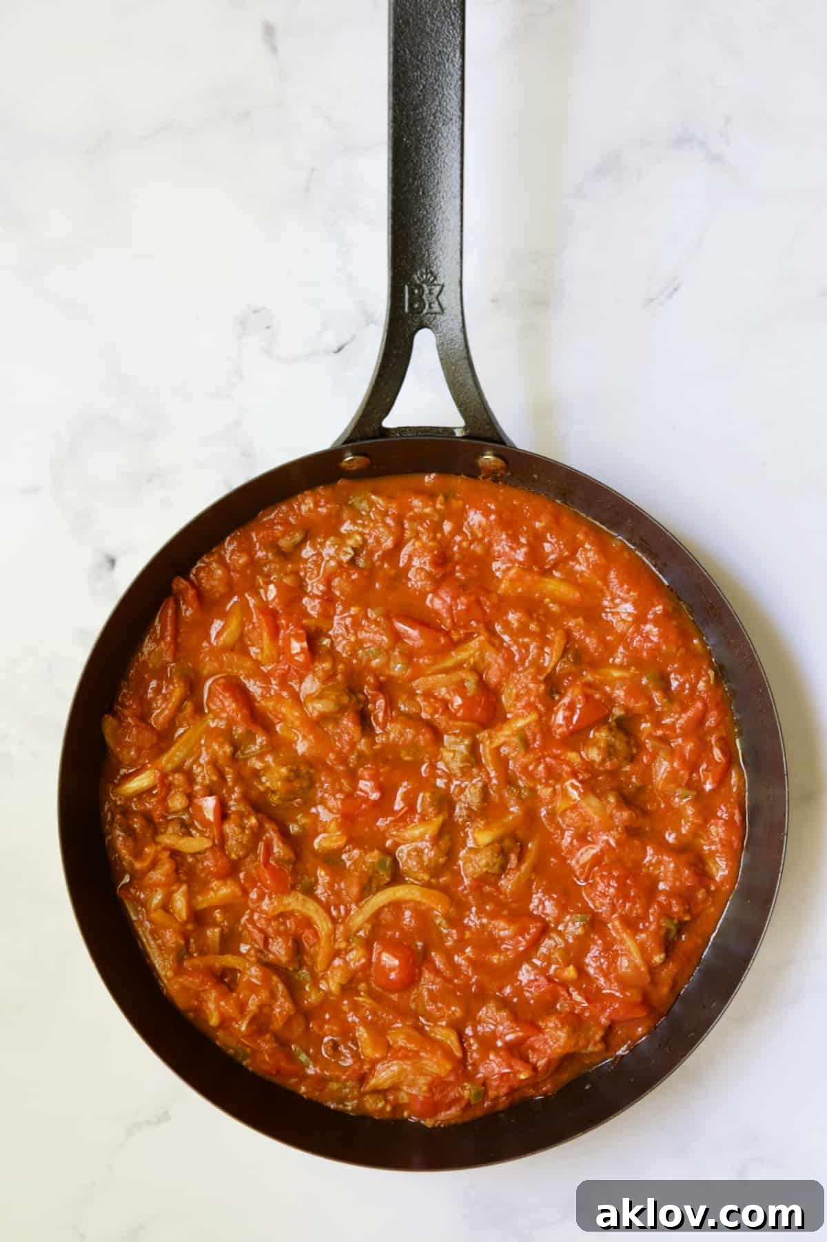 Tomato sauce with sausage in black skillet.