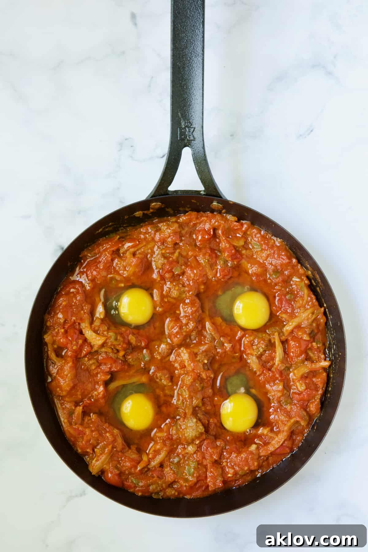 Molten Sunset Eggs 9 Four uncooked eggs carefully placed into wells created in the rich tomato and sausage sauce within a black skillet, ready for baking.