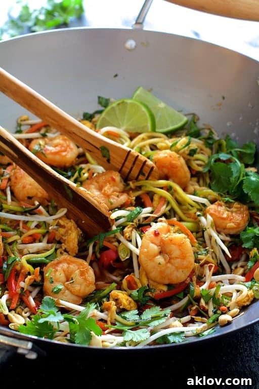 Shrimp Pad Thai with Zucchini Noodles being expertly stirred in a wok with wooden tongs, showcasing the vibrant ingredients.