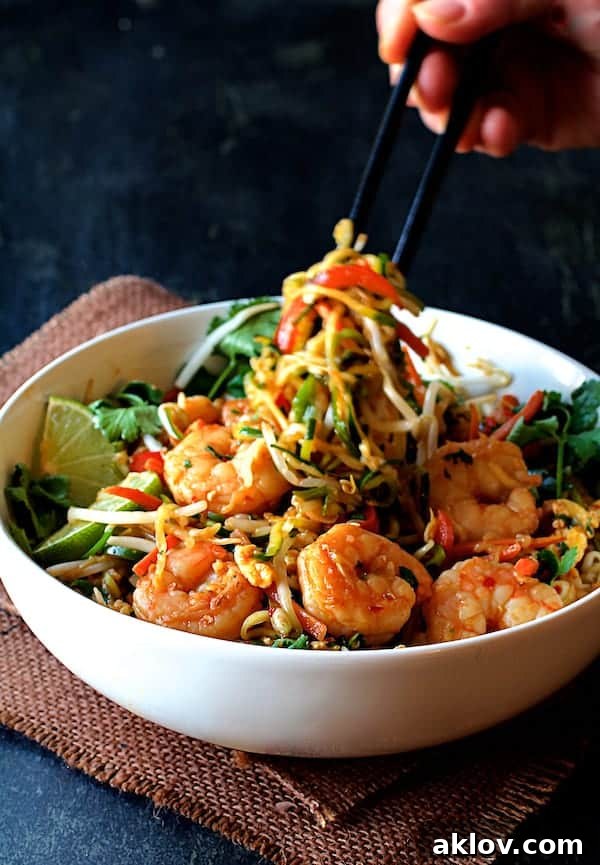 Close-up shot of Shrimp Pad Thai with Zucchini Noodles in a white bowl, with chopsticks pulling up a tangle of zucchini noodles, highlighting the texture.