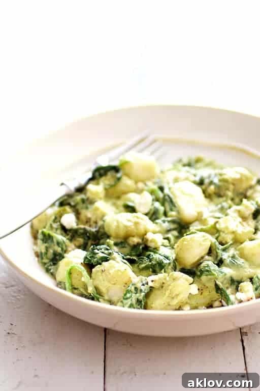 Gnocchi with Avocado Goat Cheese Sauce and Spinach served in a white bowl on a white wood background.