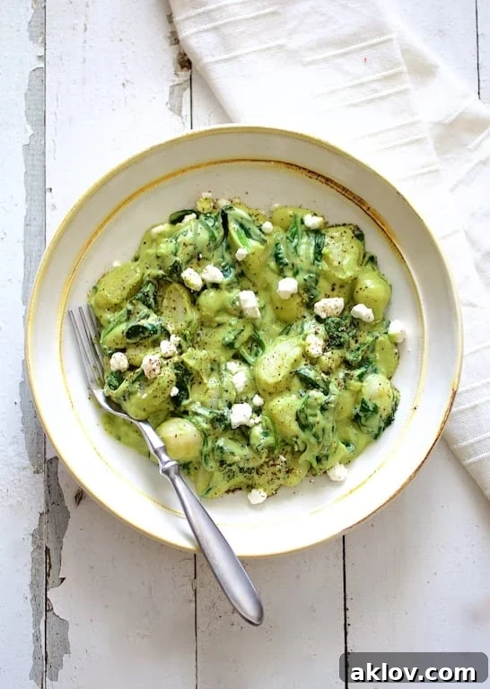 A delicious serving of gnocchi, spinach, and avocado goat cheese sauce, presented beautifully in a white bowl with a white napkin on a distressed white background.