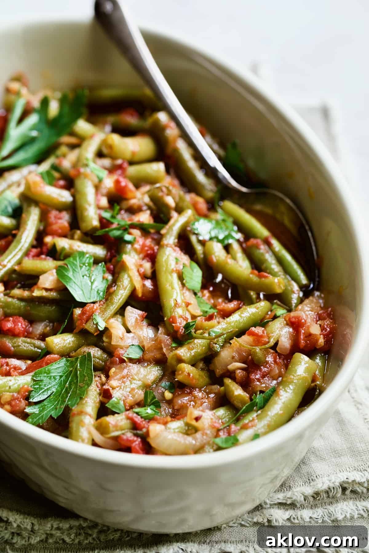 Mediterranean Green Bean and Tomato Stew 13 Mediterranean Braised Green Beans with Tomatoes in oval serving dish with serving spoon.