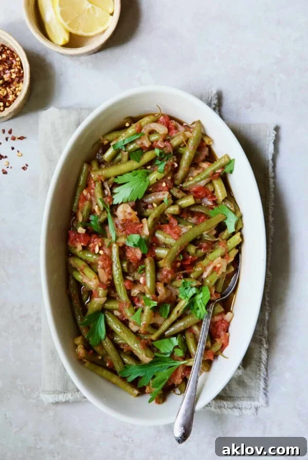 Mediterranean Green Bean and Tomato Stew 14 Mediterranean Braised Green Beans with Tomatoes in oval serving dish with serving spoon garnished with fresh parsley.