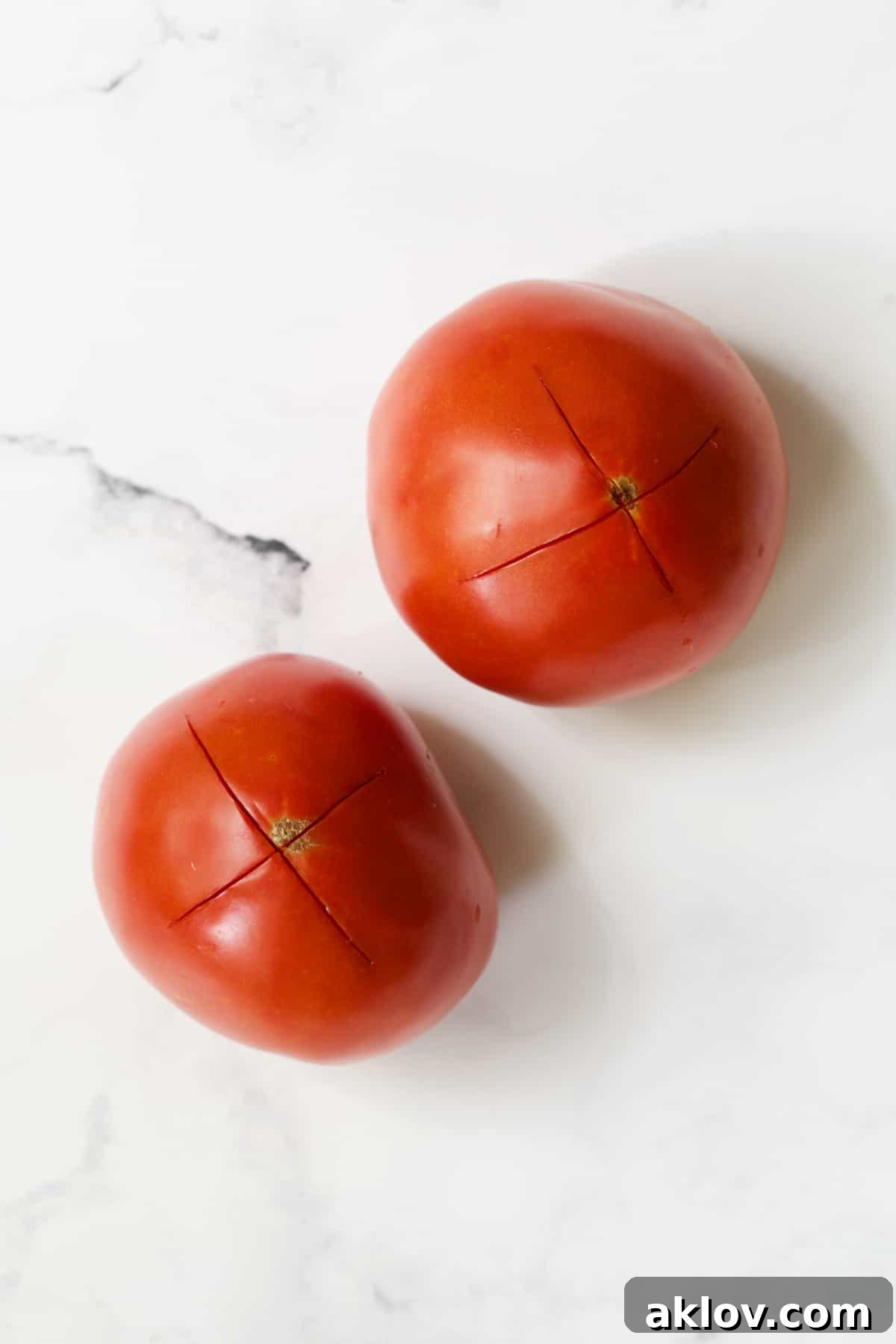 Mediterranean Green Bean and Tomato Stew 5 Two tomatoes on white background that have an X scored in the bottom.