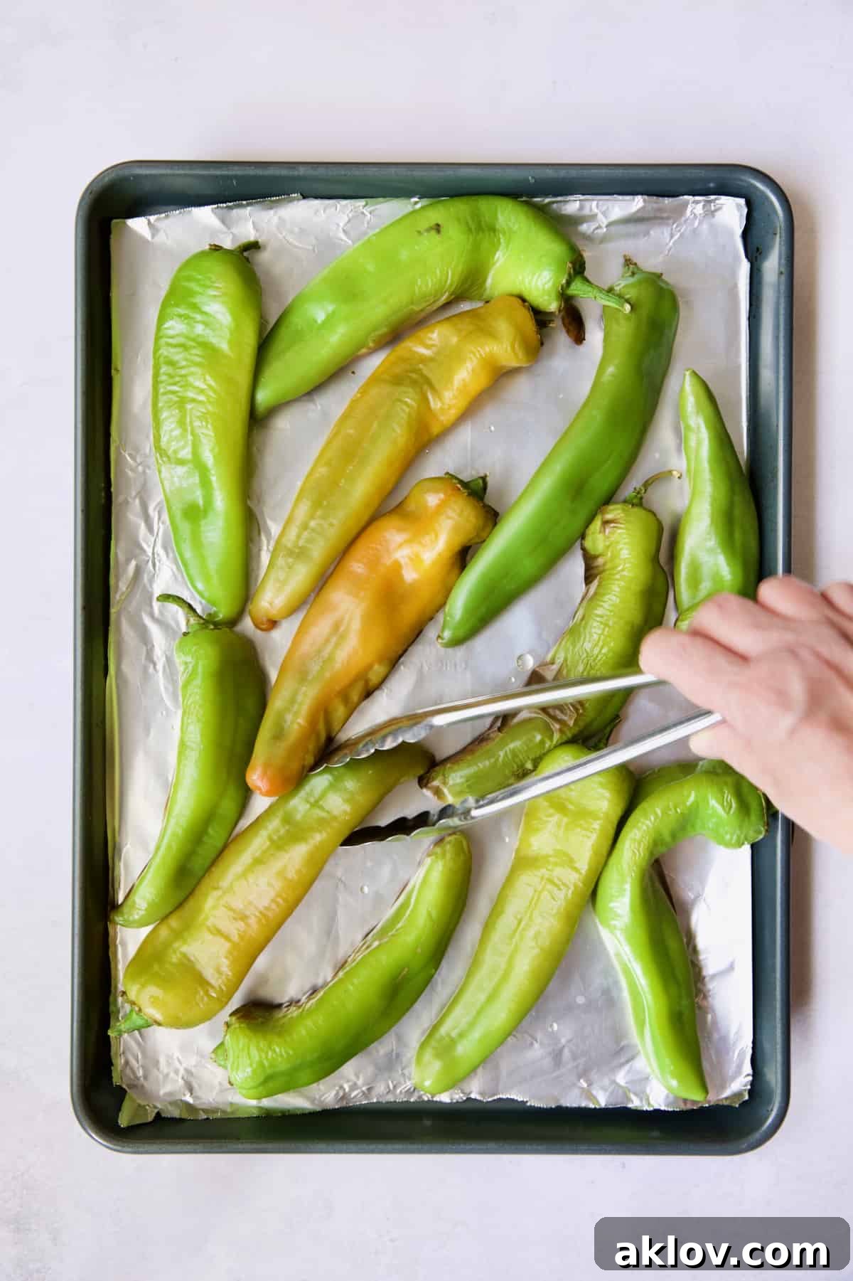 Hatch Green Chiles: Roast and Freeze for Year-Round Enjoyment 5 Hatch green chiles on a rimmed sheet pan being turned with tongs during the roasting process.