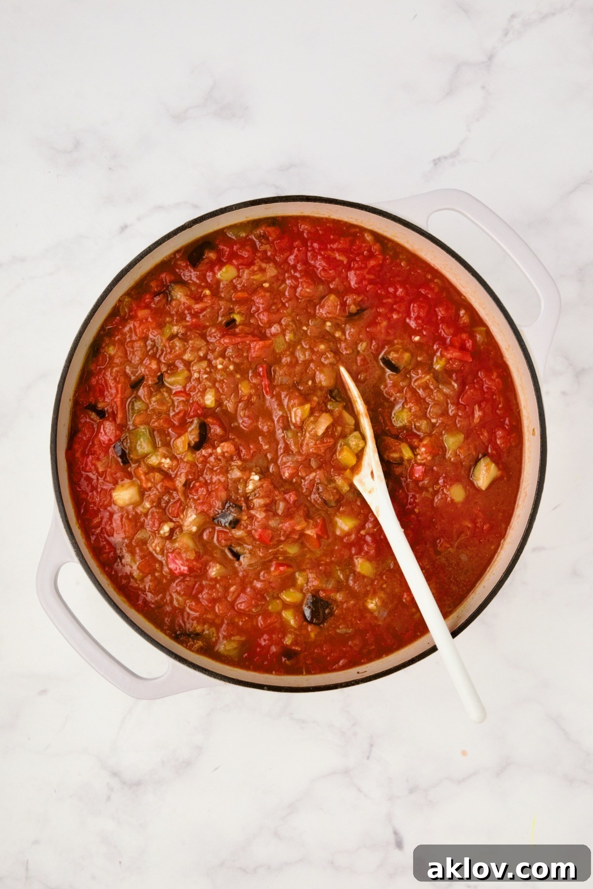 Moroccan Spiced Kofta Stew 12 Crushed tomatoes and beef broth added to vegetables in white enamel cast iron skillet.