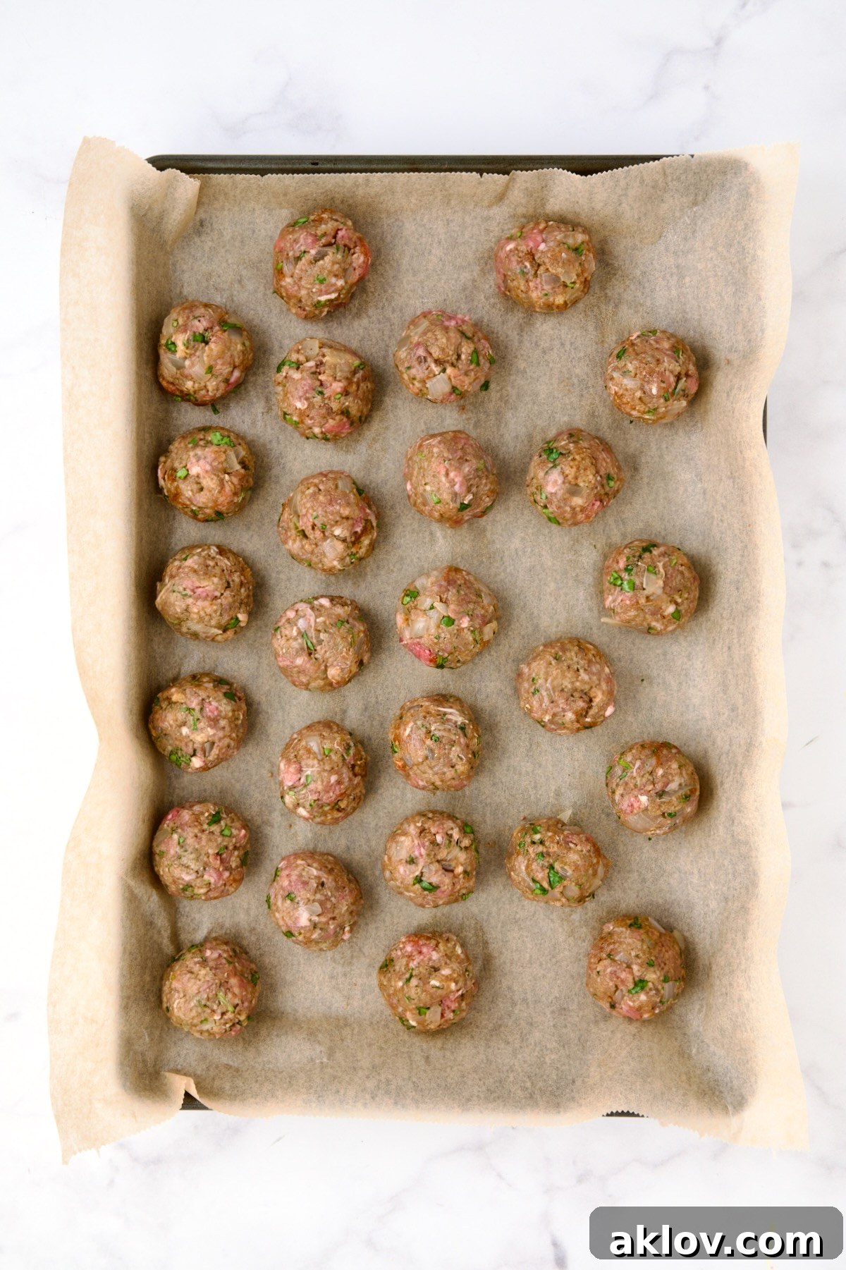 Moroccan Spiced Kofta Stew 15 26 unbaked meatballs on parchment paper lined rimmed baking sheet.