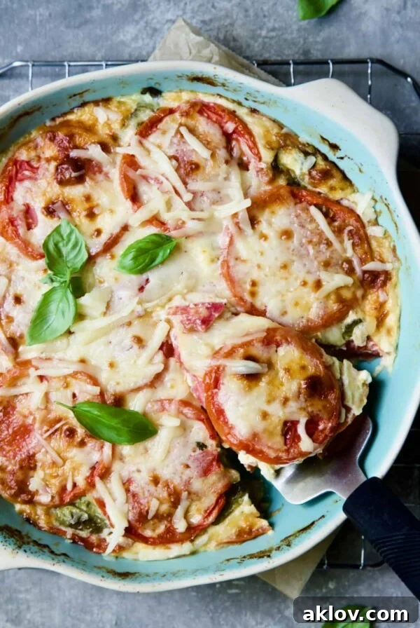 Crustless Southern Tomato Pie in light blue pie pan garnished with fresh basil with a piece cut out and about to be served.