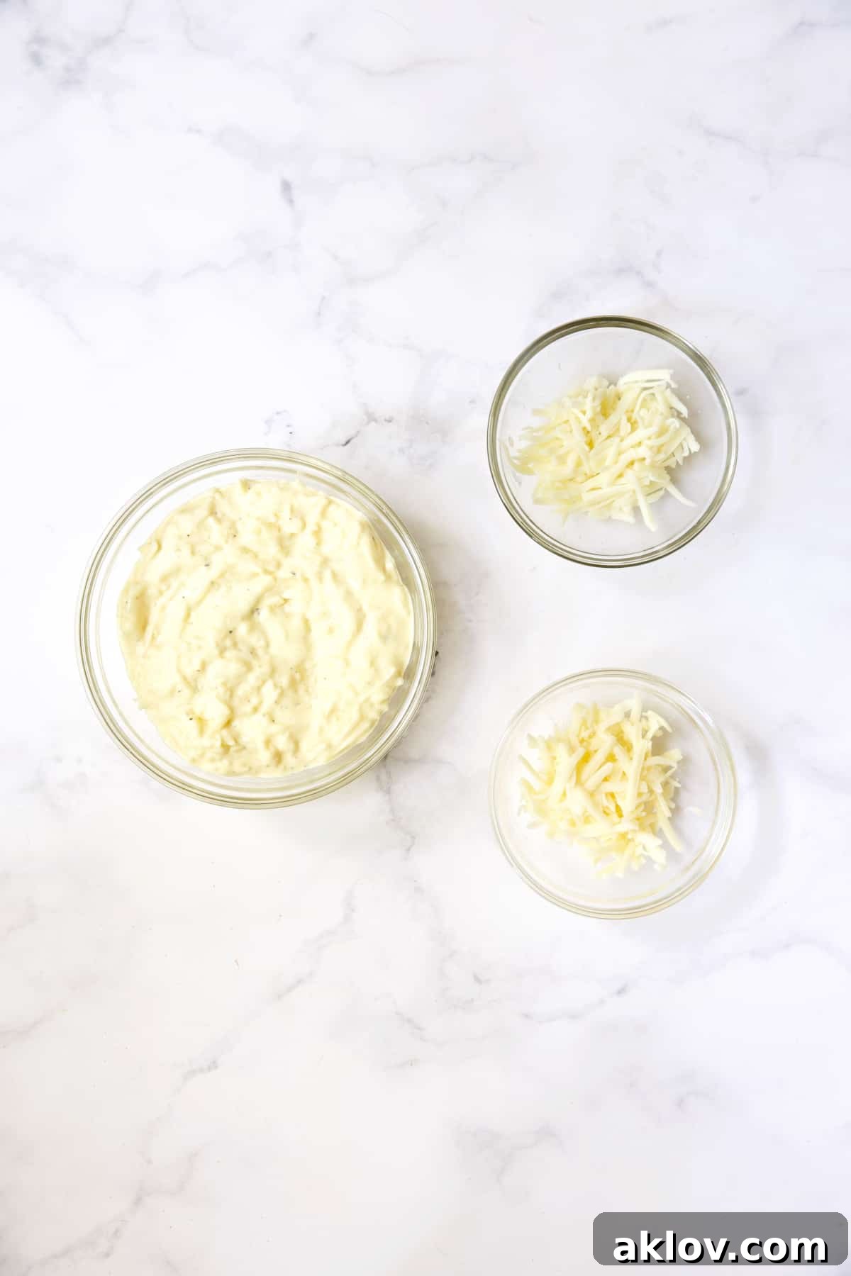 Mayonnaise and cheese mixture in glass bowl with two small bowls of cheese.