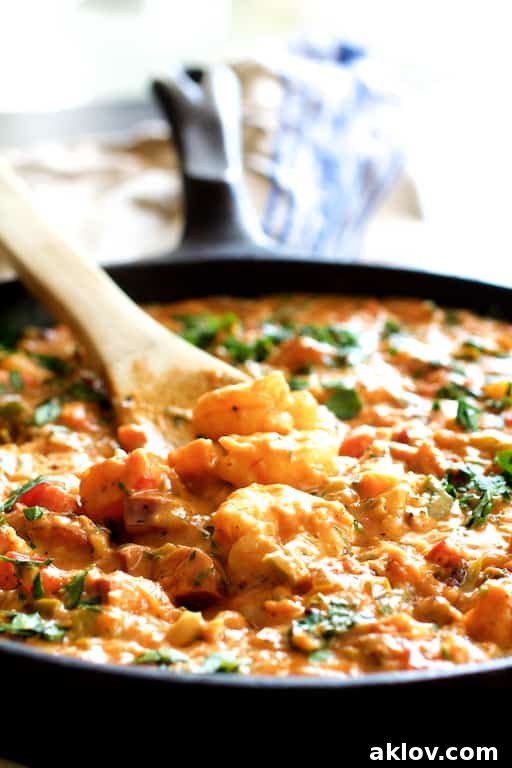Photo of Smothered Shrimp and Andouille Sausage with Creamy Parmesan Peppercorn Grits being stirred with wooden spoon in cast iron skillet.