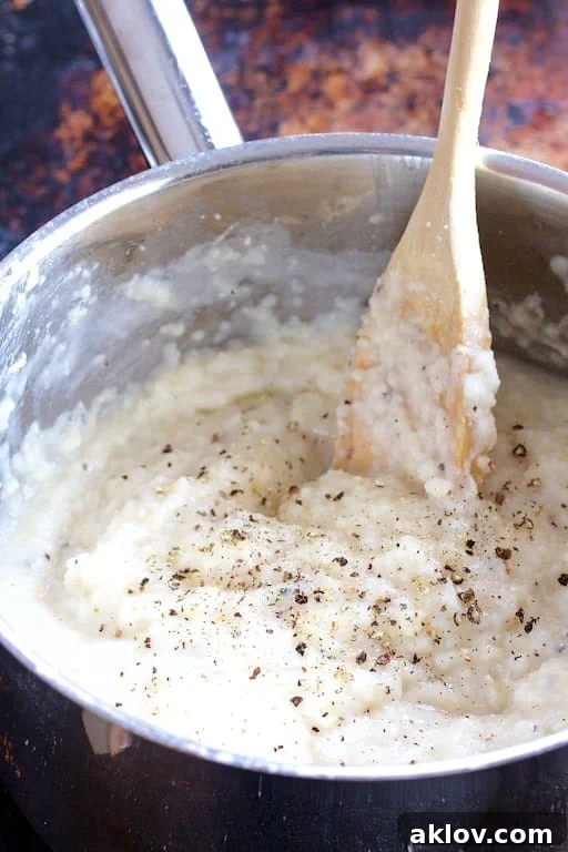 Photo of grits being cooked and stirred with wooden spoon in stainless steel saucepan.