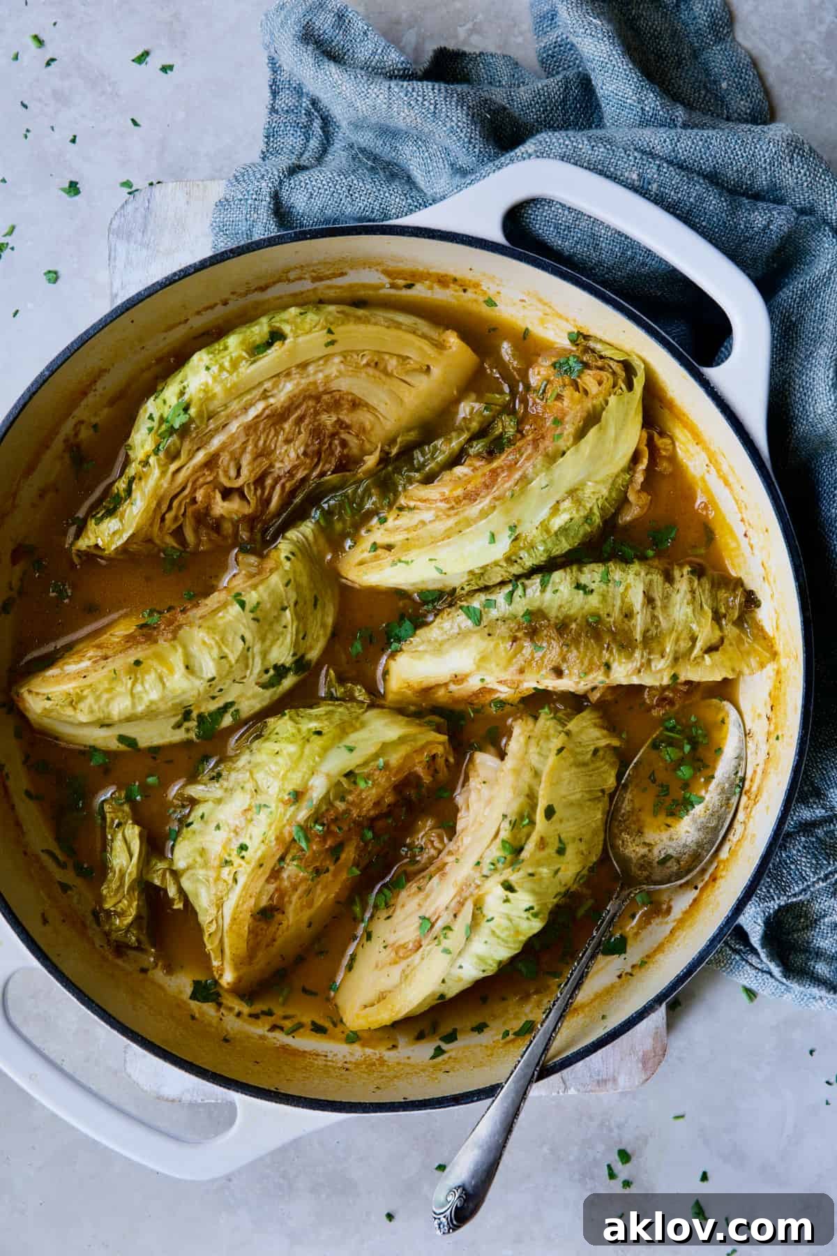 Cider Vinegar Braised Cabbage Wedges artfully arranged in a white enamel cast iron skillet, with a blue napkin nearby, ready to be served.