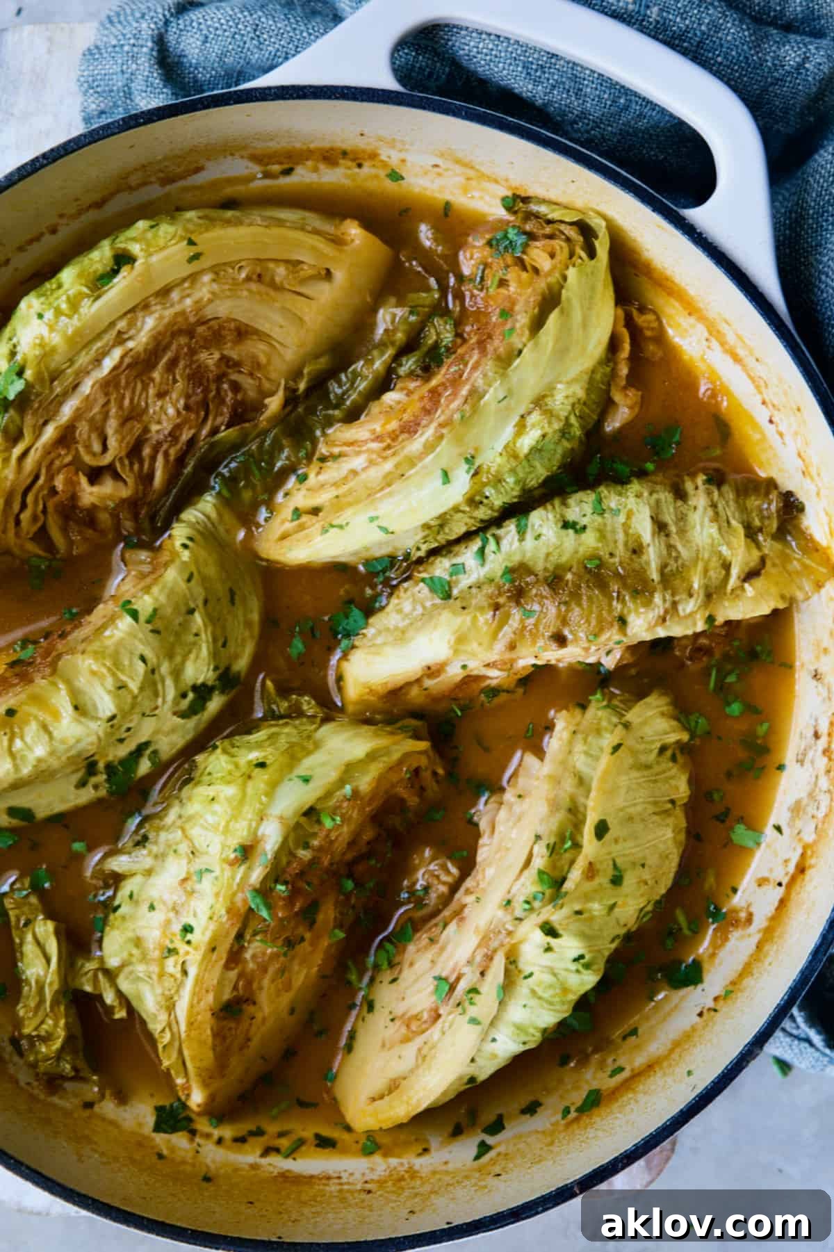 Cider Vinegar Braised Cabbage Wedges, garnished with vibrant fresh parsley, presented in a white enamel cast iron skillet.