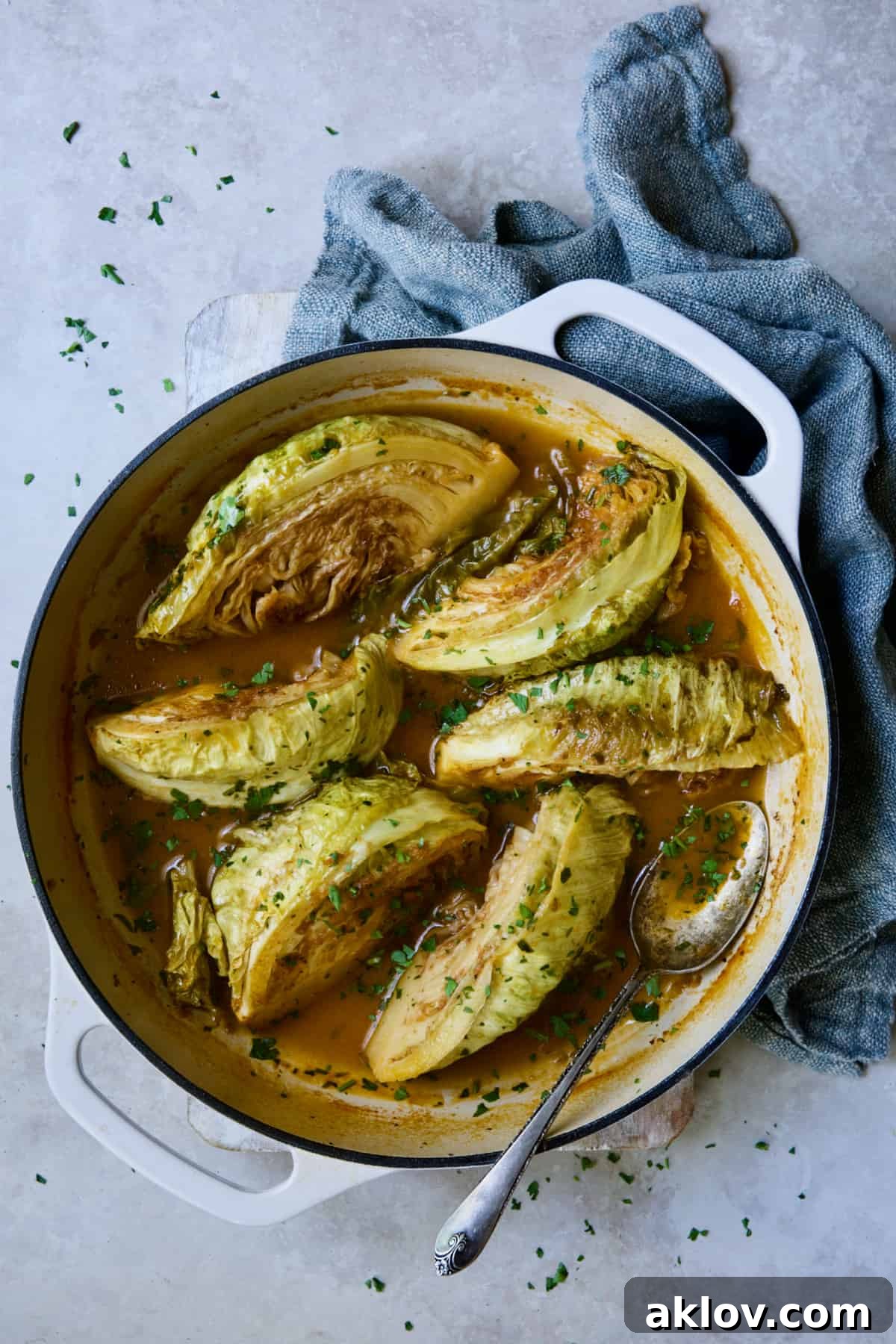 Another perspective of Cider Vinegar Braised Cabbage Wedges, glistening with sauce and garnished with parsley, served in a white cast iron skillet.