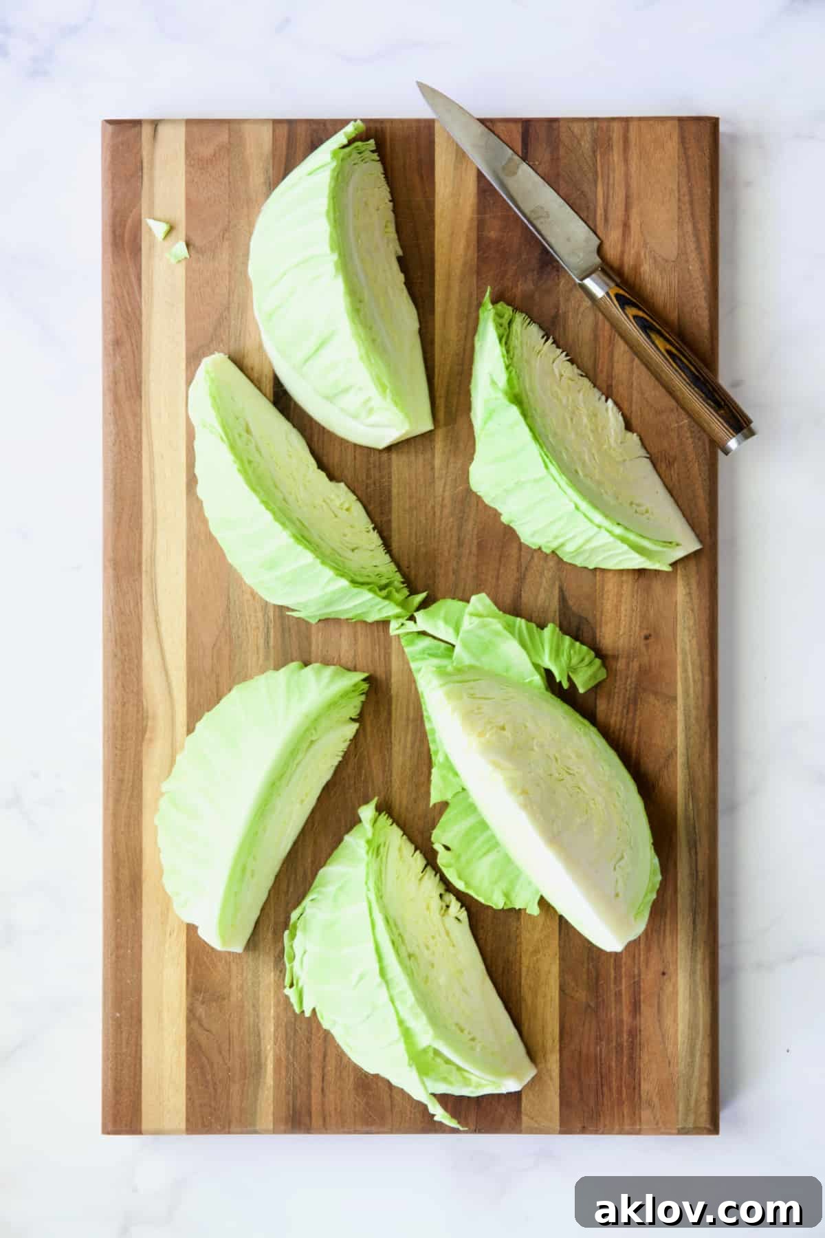 Six perfectly cut cabbage wedges resting on a wooden cutting board, alongside a chef's knife.