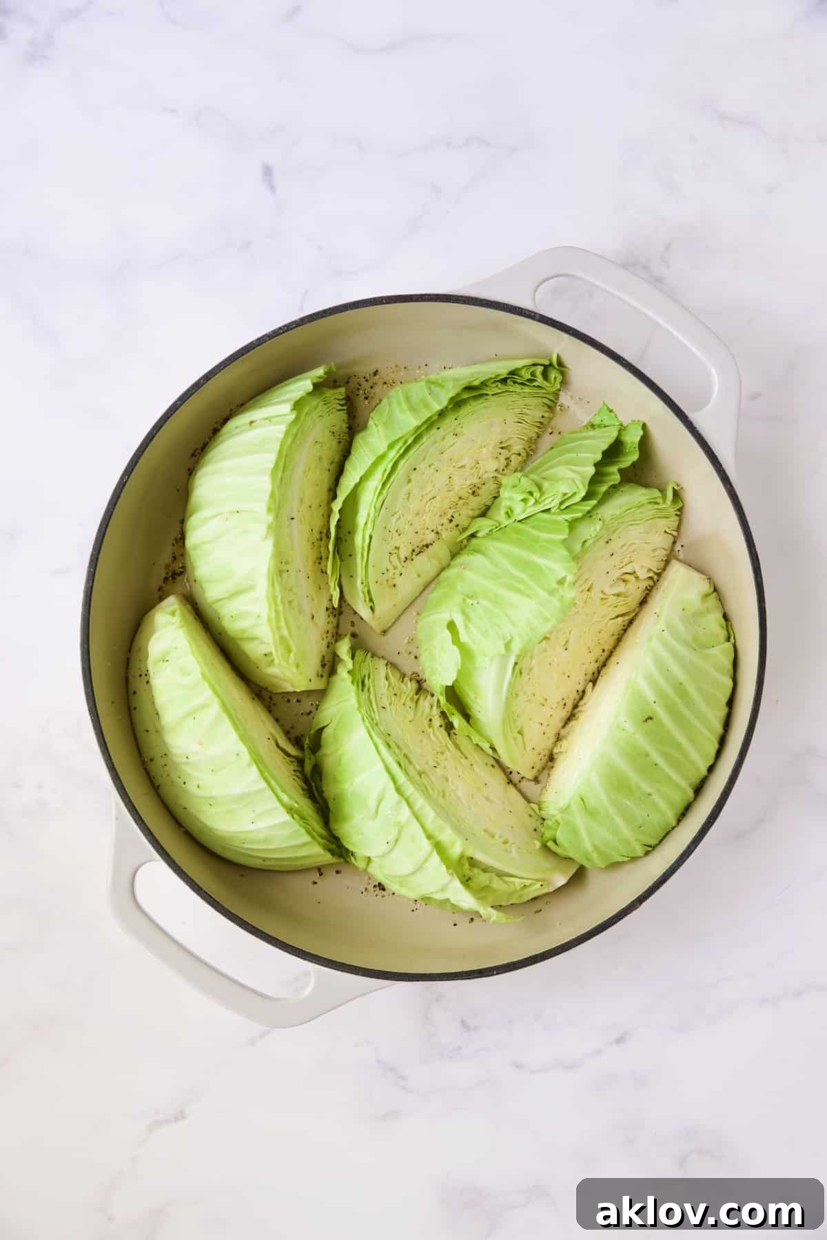 Six uncooked cabbage wedges arranged in a white enamel cast iron skillet, ready for browning.