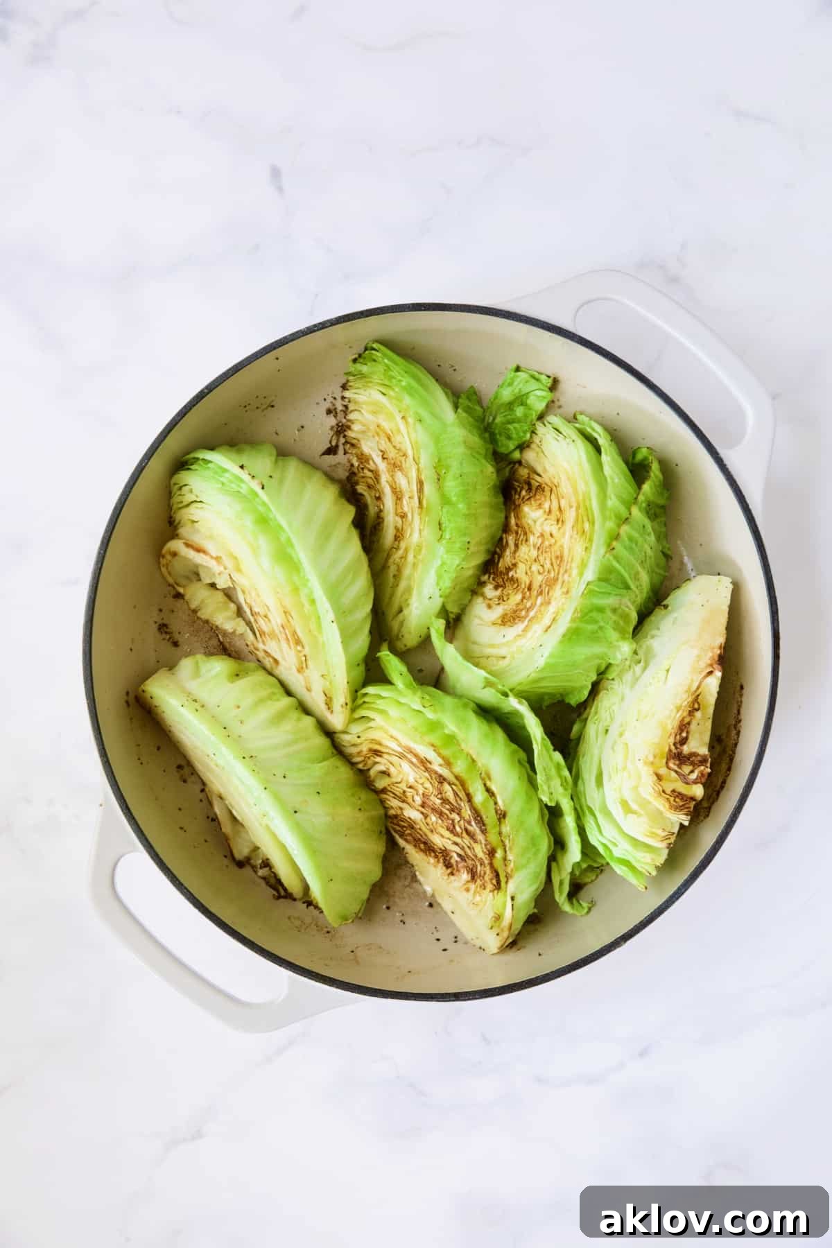 Six browned cabbage wedges in white enamel cast iron skillet.