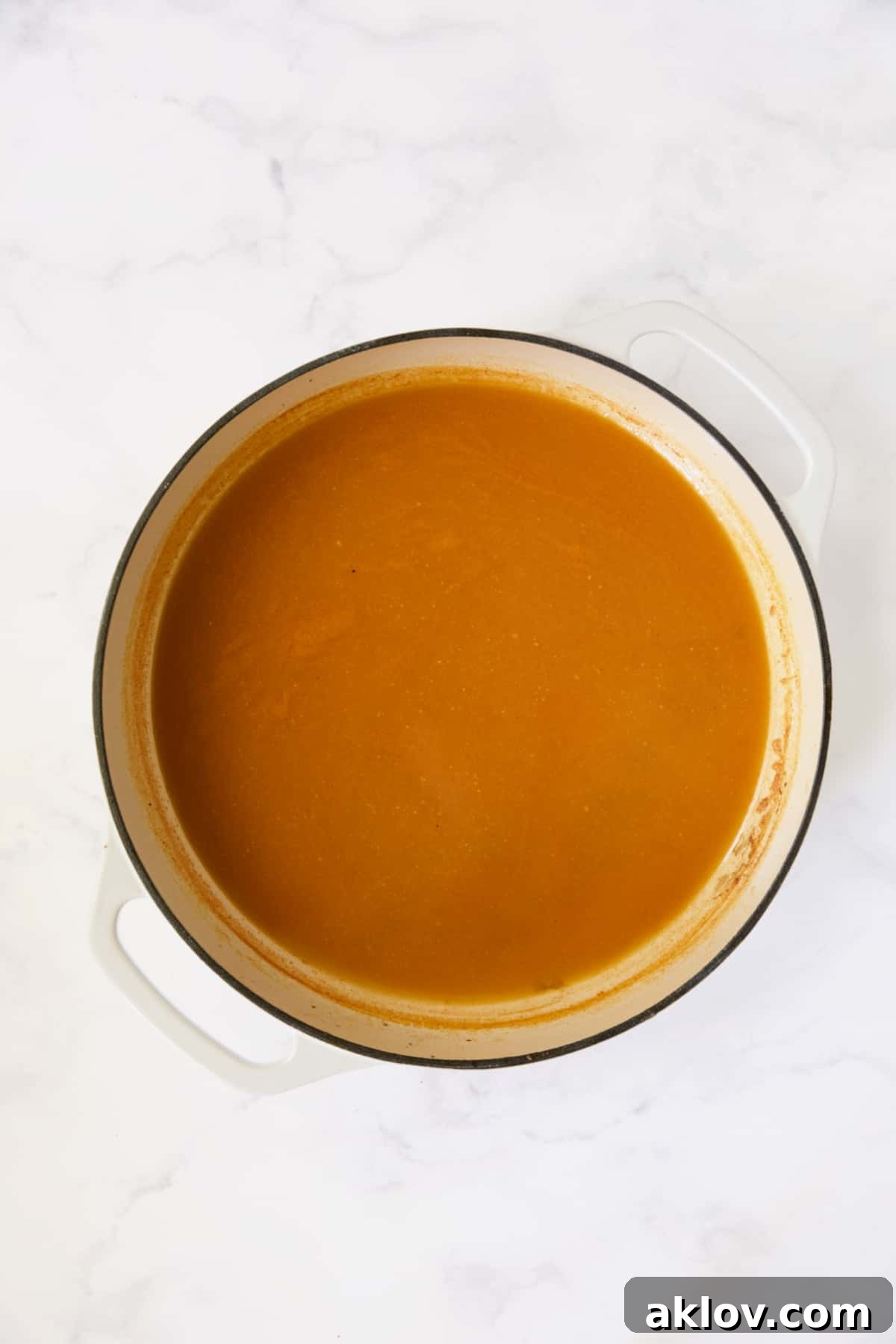 The braising sauce, now reduced and slightly thickened, simmering in a white enamel cast iron skillet.