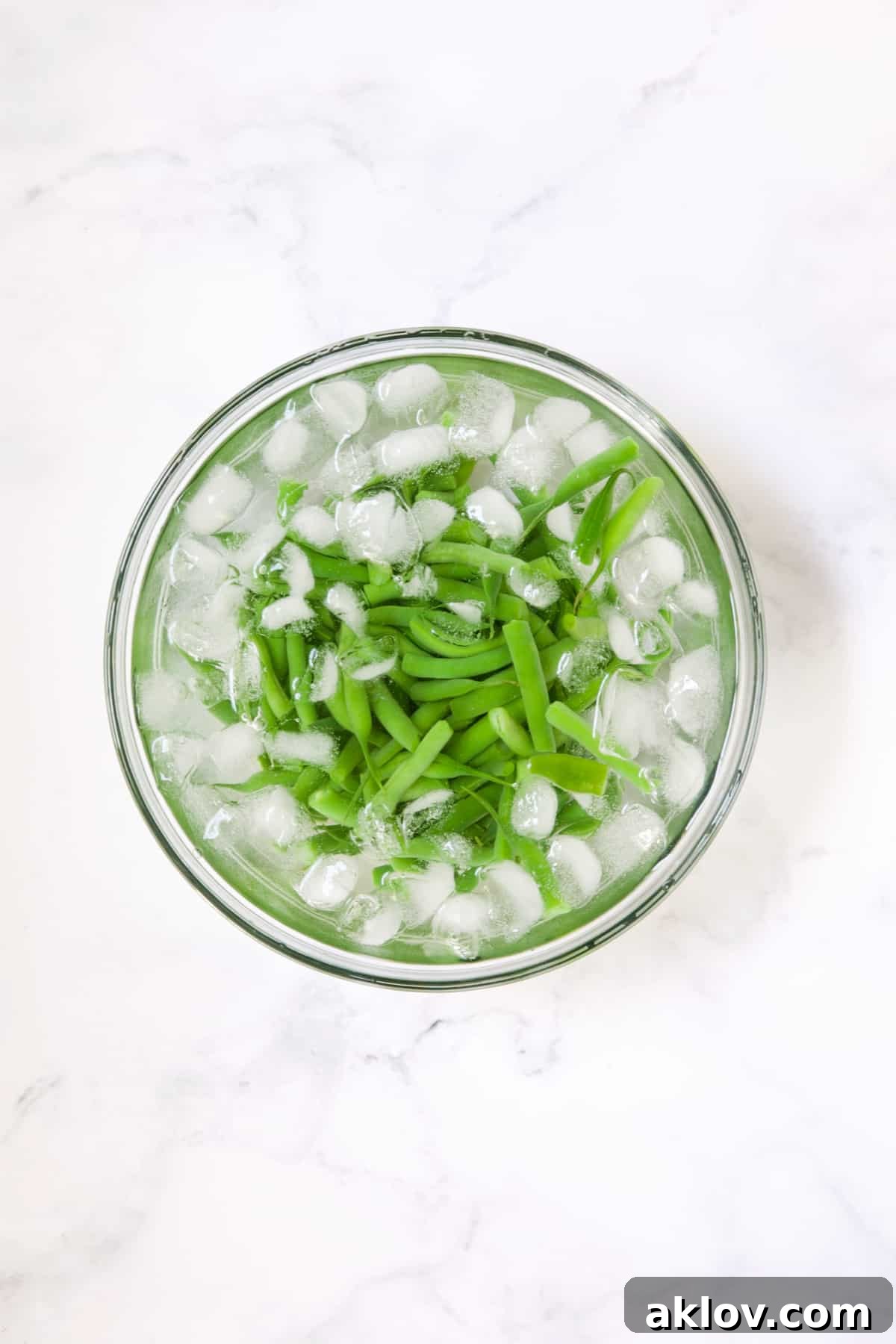 Green beans in ice water in glass bowl.