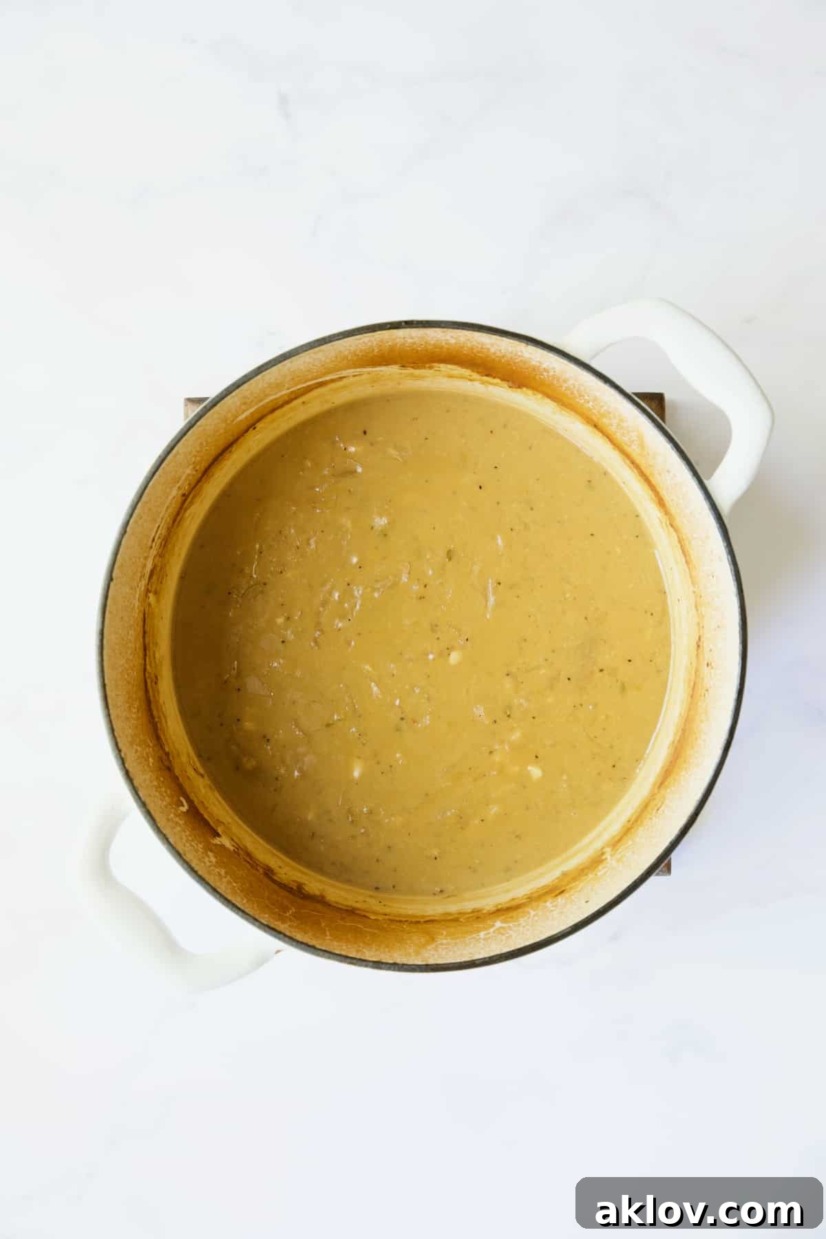 The Dijon mustard sauce thickening to a rich, glossy consistency in a white Dutch oven after the slurry has been added.