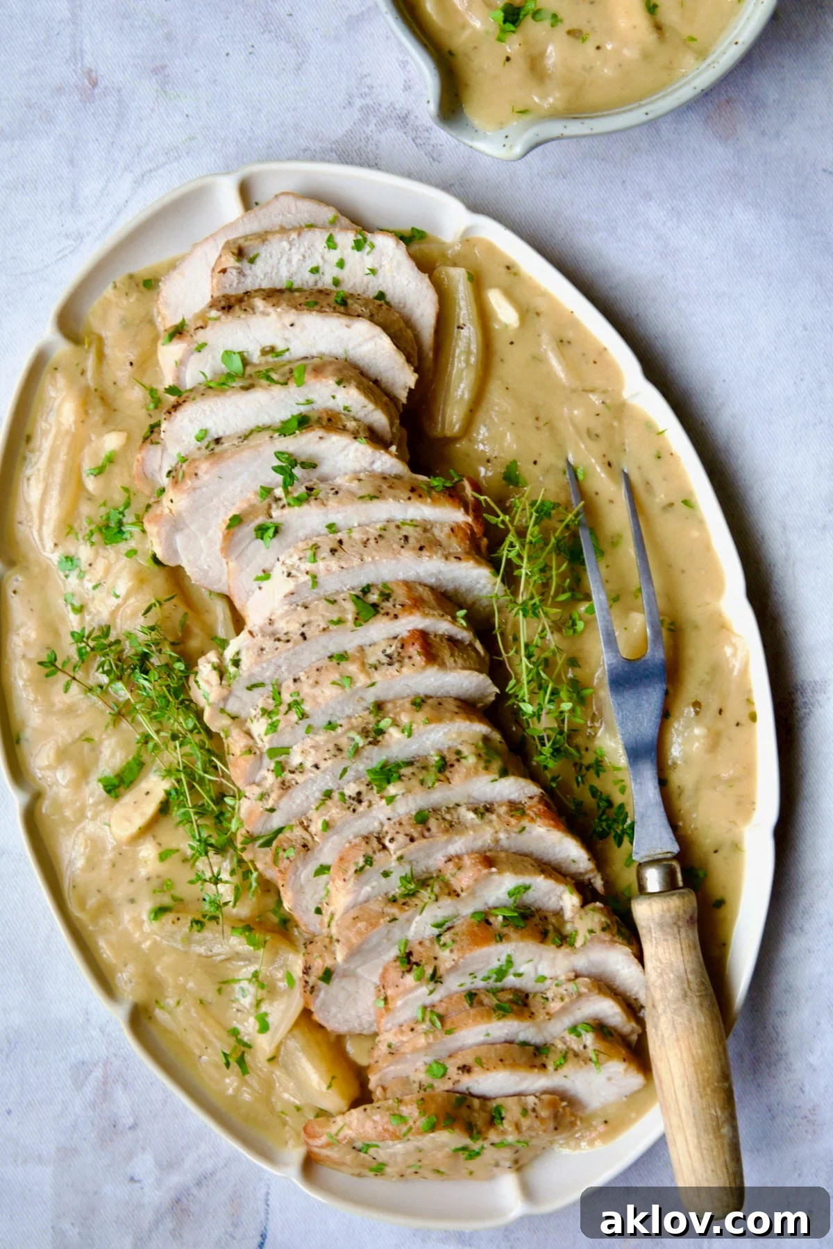 A close-up of beautifully sliced Braised Pork Loin in Dijon Mustard Sauce on an elegant scalloped oval platter, generously coated with the savory sauce and garnished with fresh thyme sprigs, ready to delight.