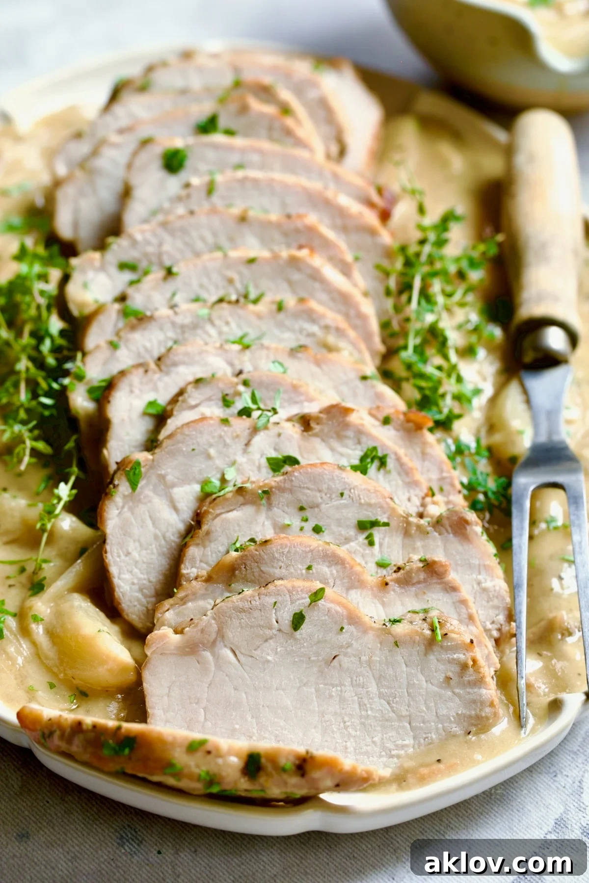 Another appealing view of the Braised Pork Loin in Dijon Mustard Sauce, artfully sliced and presented on a scalloped oval platter, garnished with fresh thyme, emphasizing its readiness for a sophisticated meal.